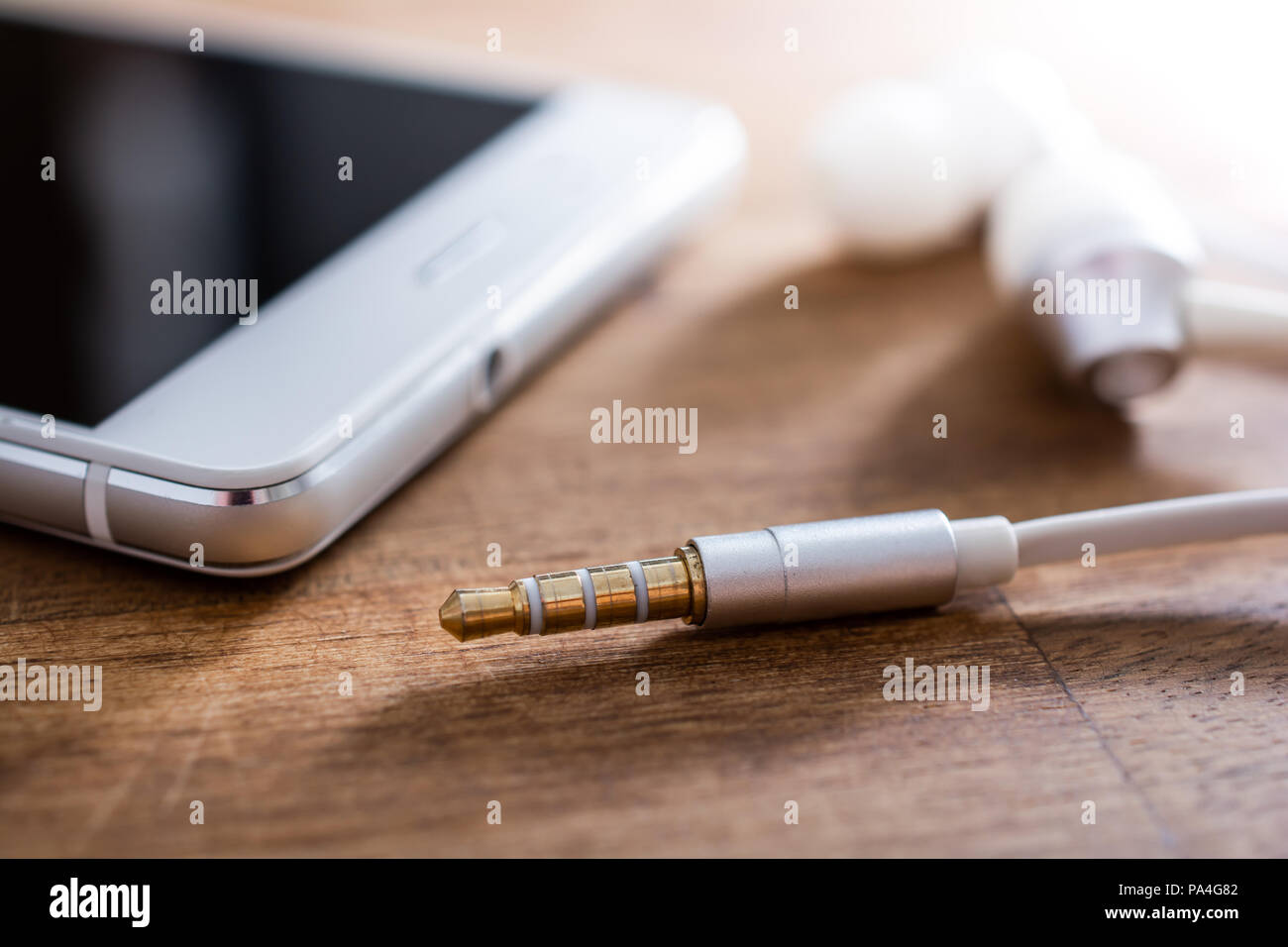 Cuffie auricolari e cavo che giace accanto a un bianco del telefono  cellulare sul tavolo di legno Foto stock - Alamy