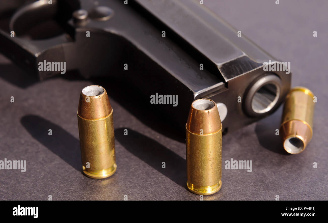 Tre punti di cava pallottole gettando ombre su uno sfondo nero accanto a una pistola di colore nero Foto Stock