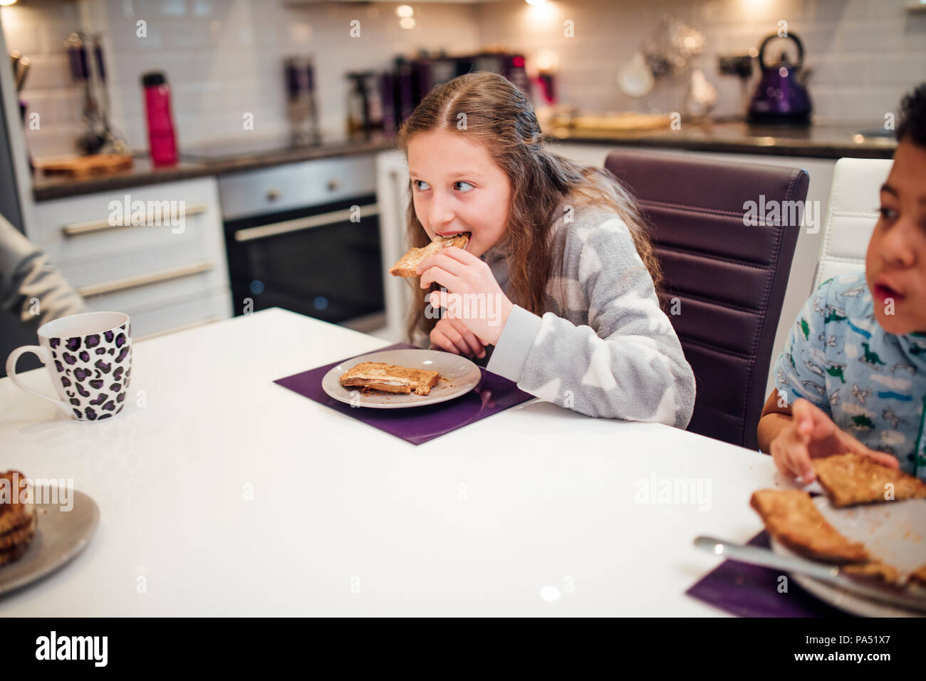Bambina è prendere un boccone di pane tostato pur avendo prima colazione con la sua famiglia a casa. Foto Stock