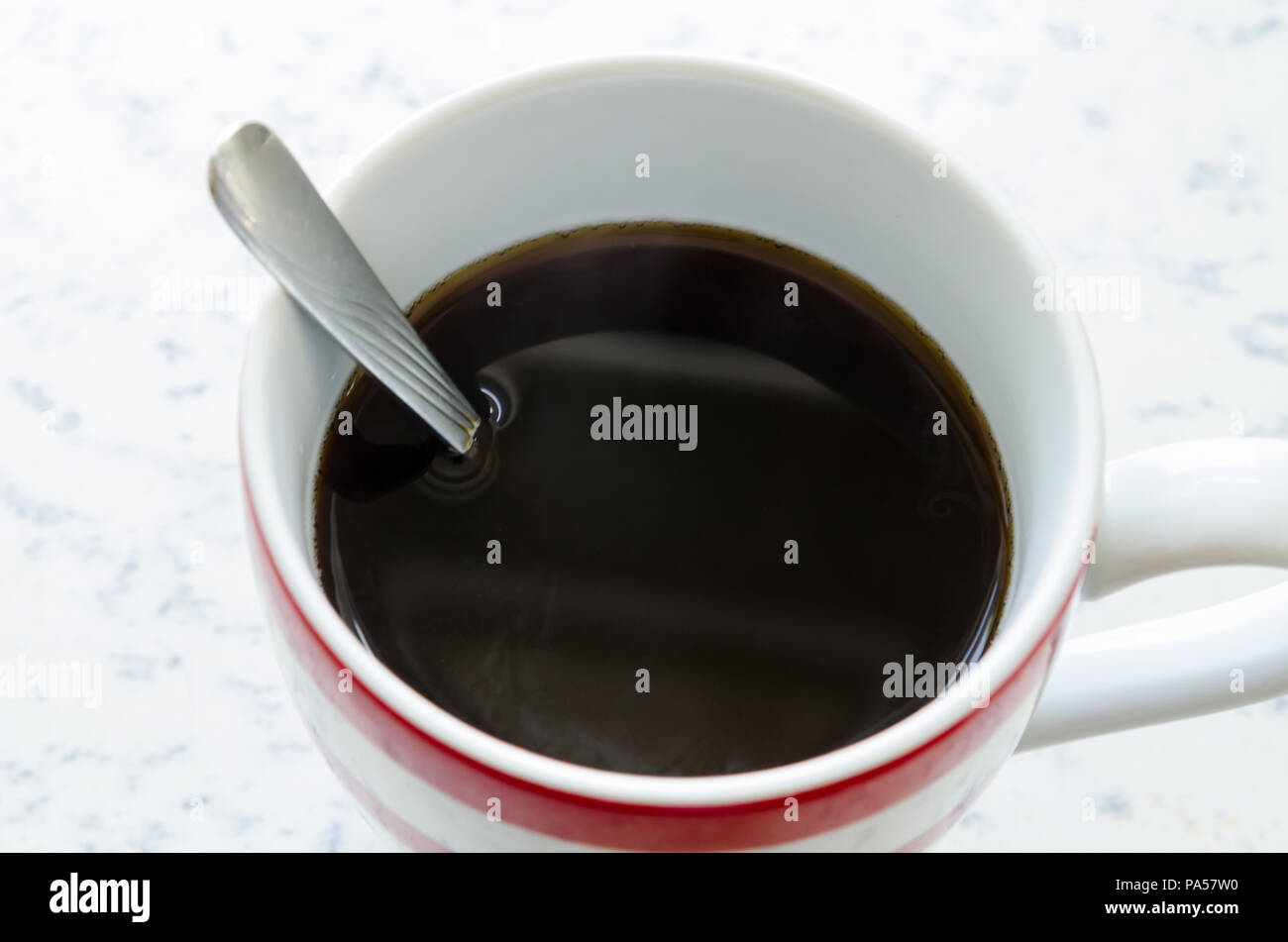 Una tazza contenente appena fatti di caffè nero con il cucchiaio ancora in coppa Foto Stock