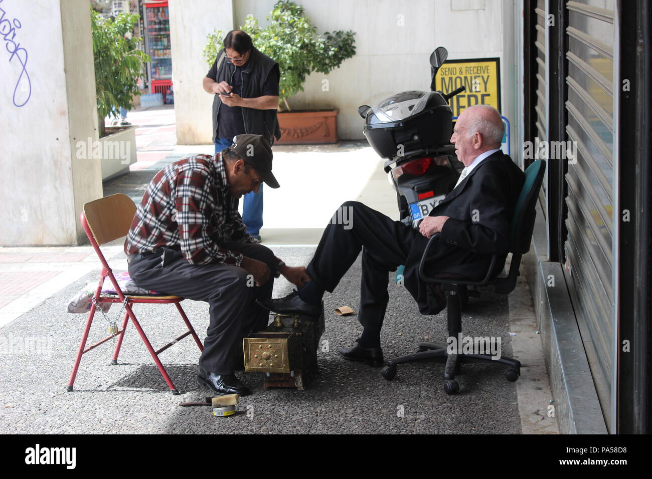 Un gentleman greco avente il servizio di pulizia scarpe su un bel giorno durante il mezzogiorno in Atene. Foto Stock