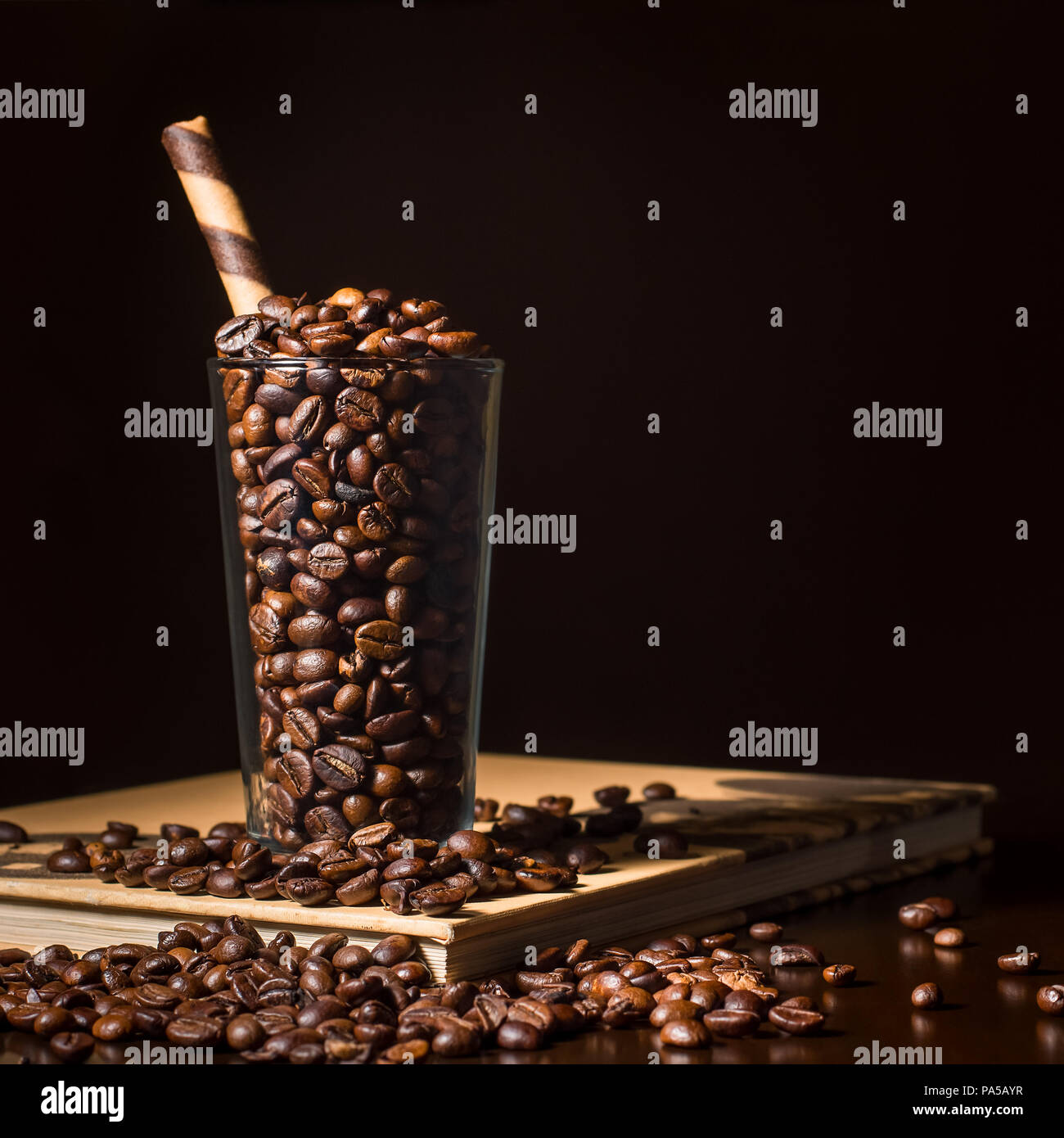 Bicchiere di chicchi di caffè sul tavolo con libro - dark e moody coffee shop scena Foto Stock
