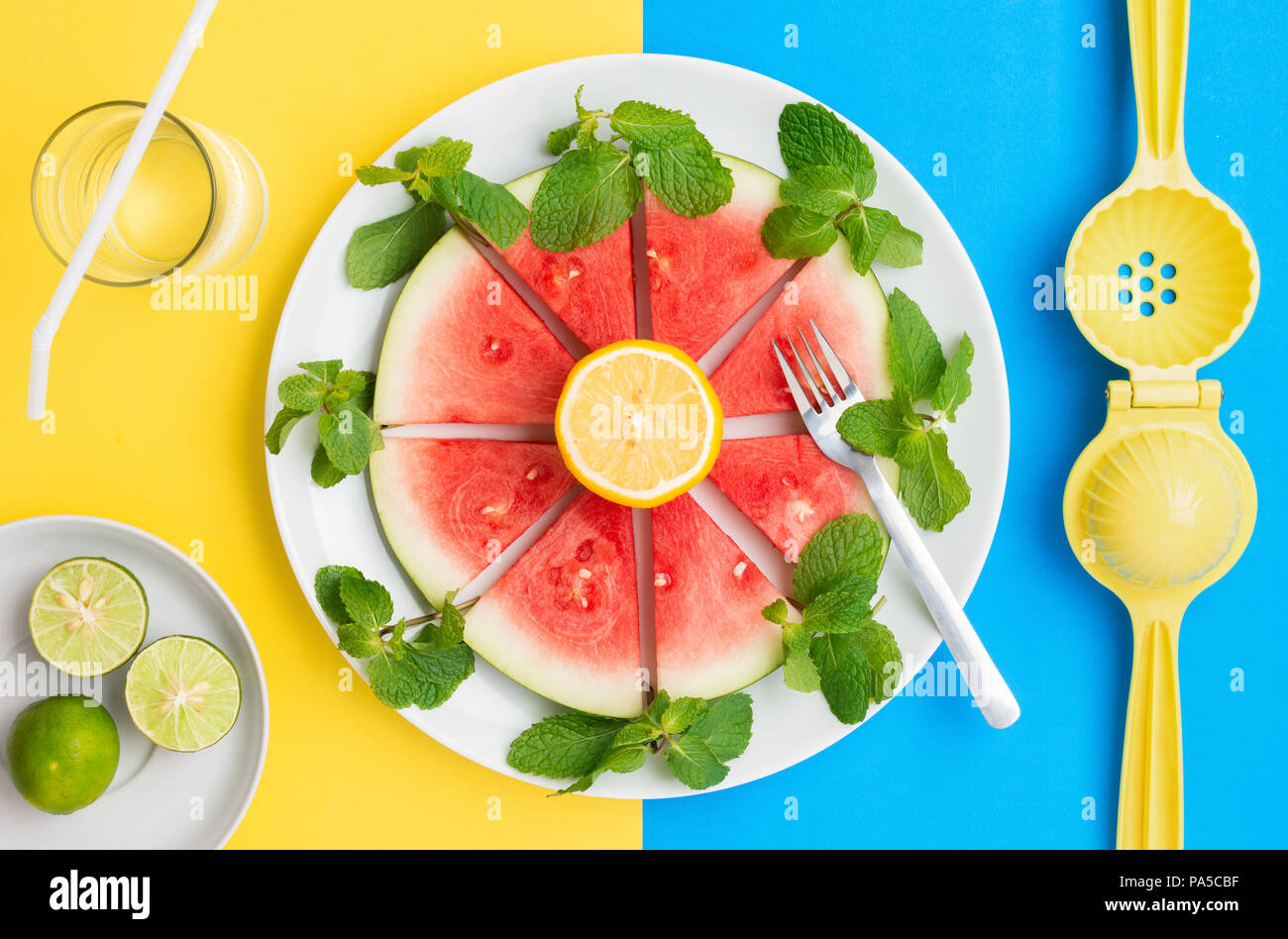 Anguria sulla piastra con limone e foglie di menta su un gruppo colore di contrasto dello sfondo. Foto Stock