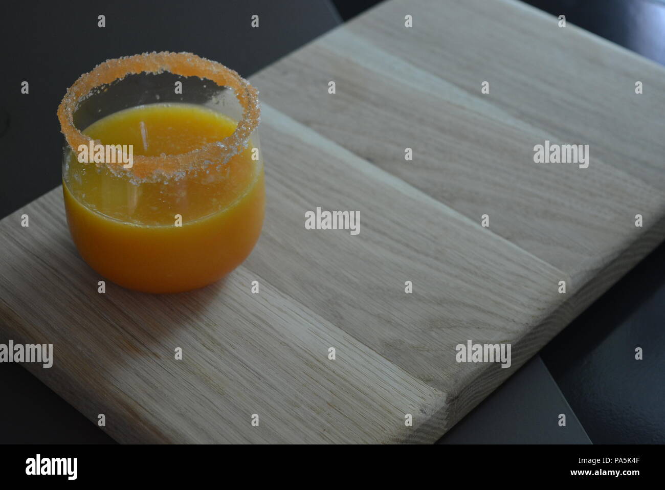 Un bicchiere di succo d'arancia con un bordo di zucchero carota su uno sfondo di legno chiaro Foto Stock