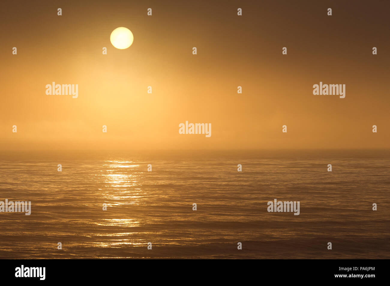 Impostazione di sole attraverso la nebbia oltre oceano pacifico Foto Stock