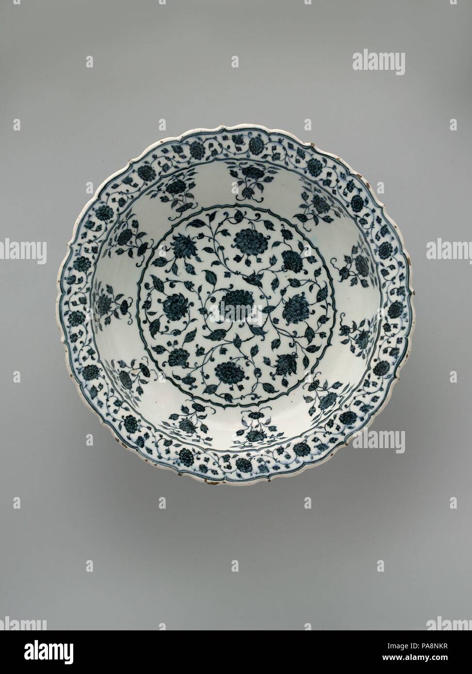 Footed piatto con Foliate Rim a imitazione della porcellana cinese. Dimensioni: H. 4 7/16a. (11,3 cm) Diam. 14 1/4 in. (36,2 cm). Data: ca. 1570-80. Molti sultani ottomani furono appassionati collezionisti di porcellane cinesi e l'importazione di tali merci hanno avuto un profondo effetto sul livello regionale della produzione di ceramica. I cartigli floreali, foliate rim e tavolozza di questo Iznik ciotola riproducono quelli di un quindicesimo secolo prototipo cinese. L'insolita aggiunta di un piede sollevato su questo pezzo, tuttavia, sembra essere un ottomano trovato. Museo: Metropolitan Museum of Art di New York, Stati Uniti d'America. Foto Stock