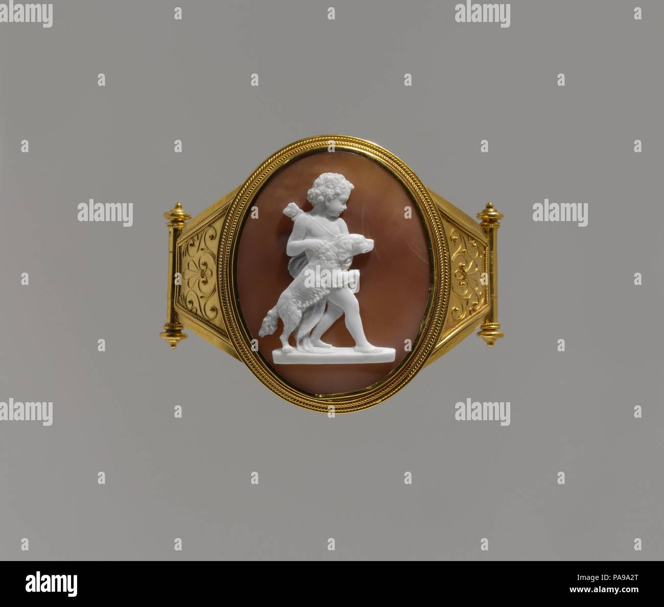 Amorino con un cane. La cultura italiana, Roma. Dimensioni: complessivo: 2 3/16 x 2 3/4 x 2 5/8a. (5,6 x 7 x 6,7 cm); visibile cameo (conferma): 48,3 x 38 mm. Autore: Luigi Saulini (Italiano, 1819-1883). Data: 1860-70. Luigi Saulini era un hardstone carver di grande destrezza. Egli ha più frequentemente prodotte cammei di shell, per la quale è addebitato un decimo del prezzo. La maggior parte della sua produzione era basata su statue dai suoi contemporanei. Il modello qui è stato un non ancora identificato il gruppo di marmo nel round (indicata con lo zoccolo in fondo). Il bracciale, insieme con un altro visualizzando un micromosaic circlet di Itali Foto Stock