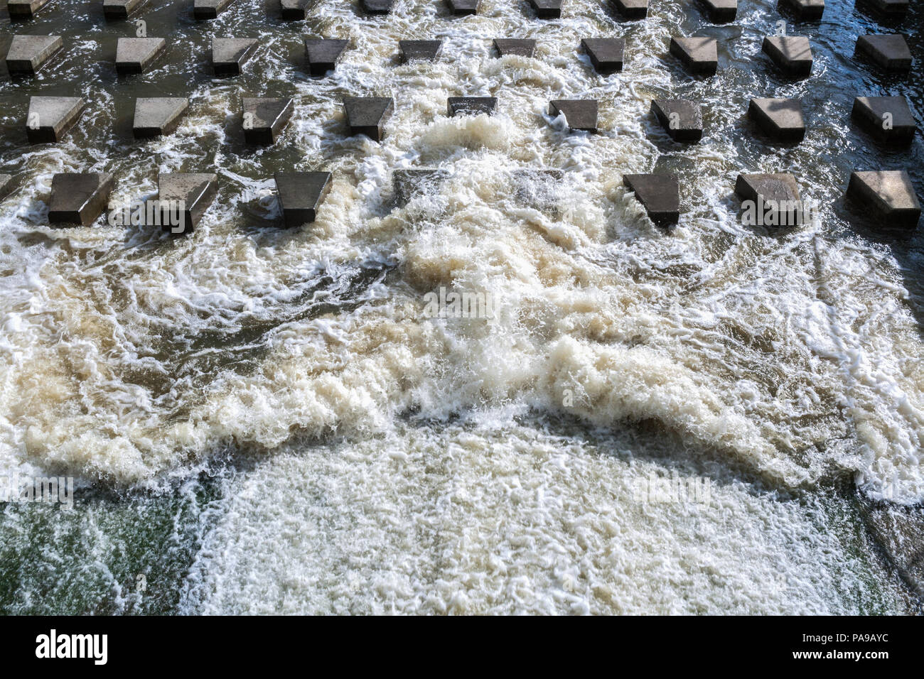 Potente flusso di acqua di schiumatura si blocca su calcestruzzo pietre-frangiflutti vicino alla diga. Foto Stock