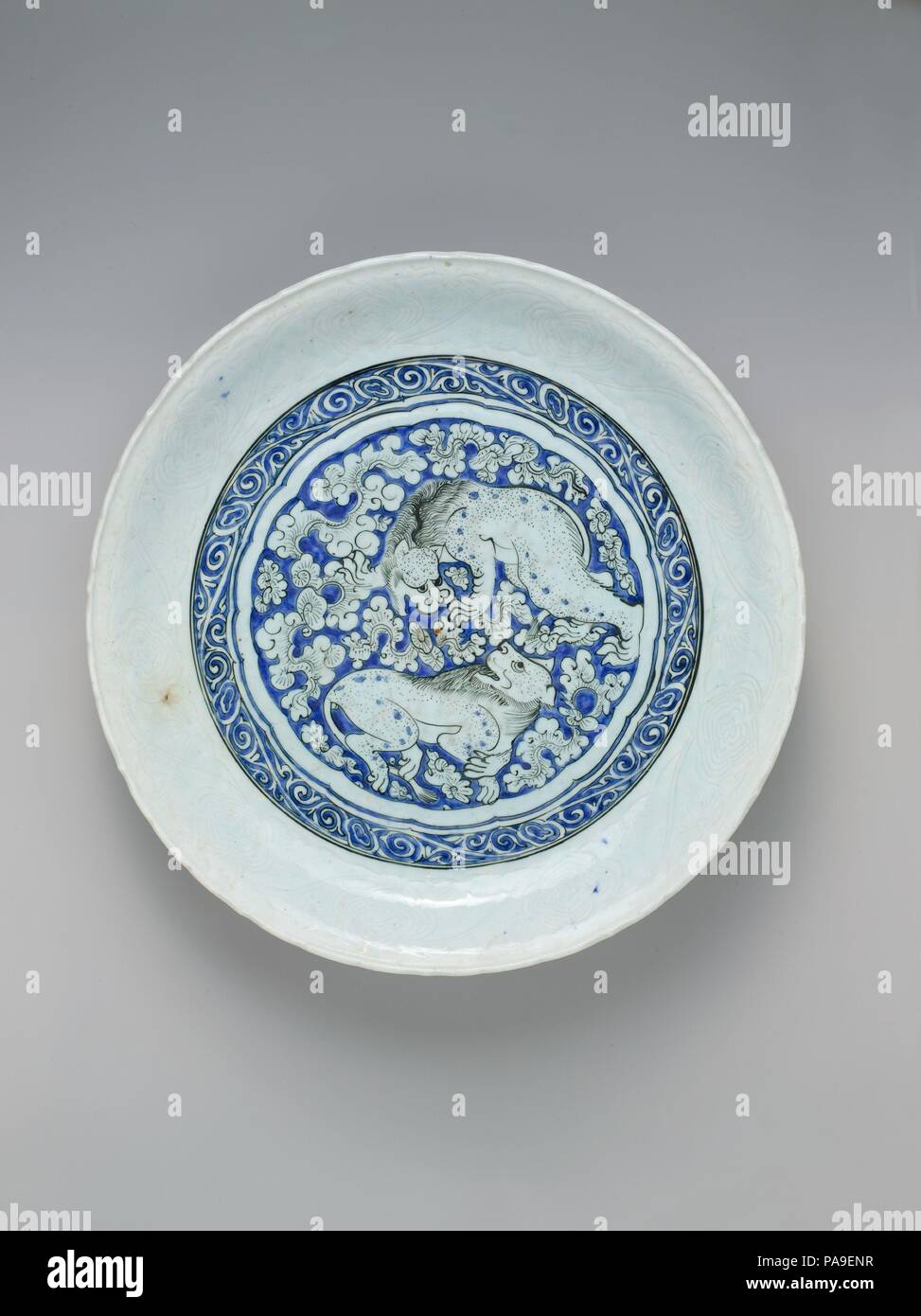 Piatto con due leoni di combattimento. Dimensioni: H. 3 1/4 in. (8.3 cm) Diam. 17 1/16 in. (43,4 cm). Data: ca. 1635. Nel secondo quarto del XVII secolo, Cinese blu-bianca porcellana la produzione è diminuita e iraniani di vasai intensificato la produzione cinese di-ispirato bianco e blu in ceramica. I due leoni, il vorticoso nuvole carnosa con il loro aspetto vegetale e la ripetizione di scorrere tutti i alludono a blu-bianco esportazione cinese ware. Museo: Metropolitan Museum of Art di New York, Stati Uniti d'America. Foto Stock