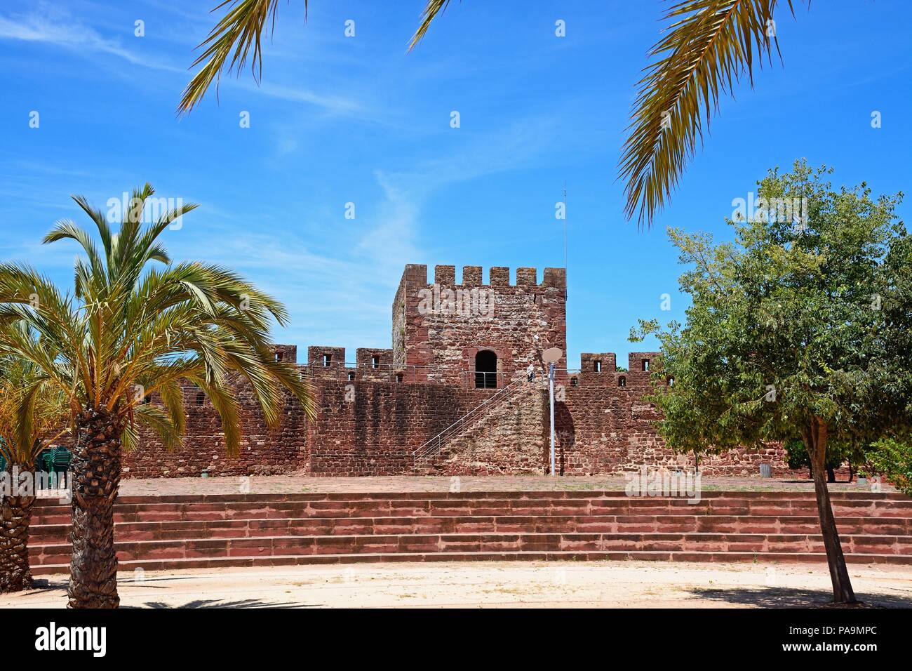 Palme e giardini paesaggistici entro il castello medievale con merli e torre al posteriore, Silves, del Portogallo, dell'Europa. Foto Stock