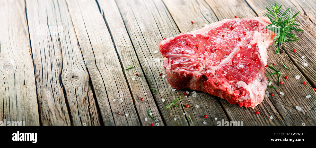 Materie T-Bone Steak su legno con rosmarino e pepe rosa Foto Stock