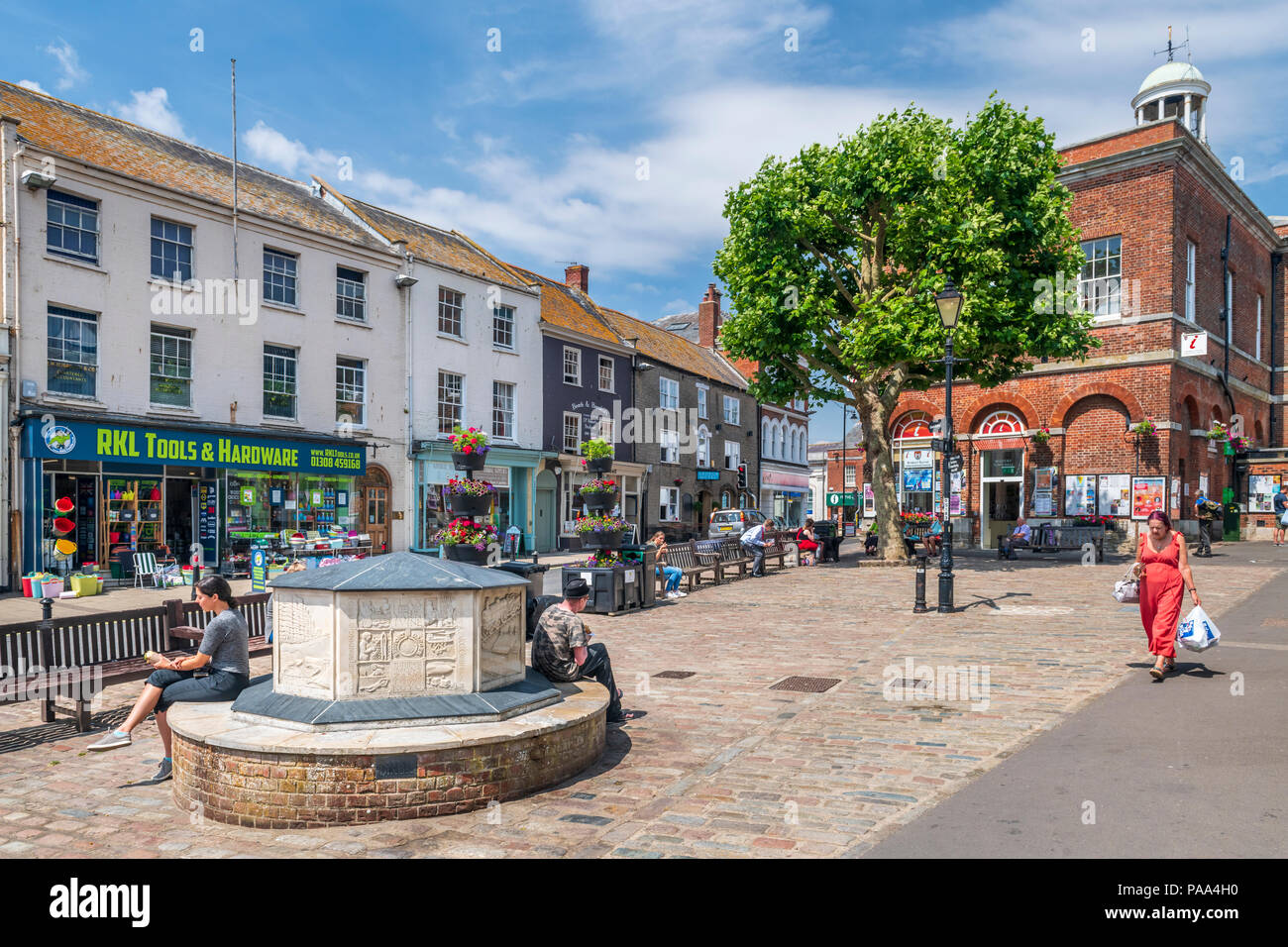 In un caldo pomeriggio nel Luglio, agli acquirenti di godersi il sole in piazza a Bridport al di fuori del centro di informazioni turistiche. Foto Stock