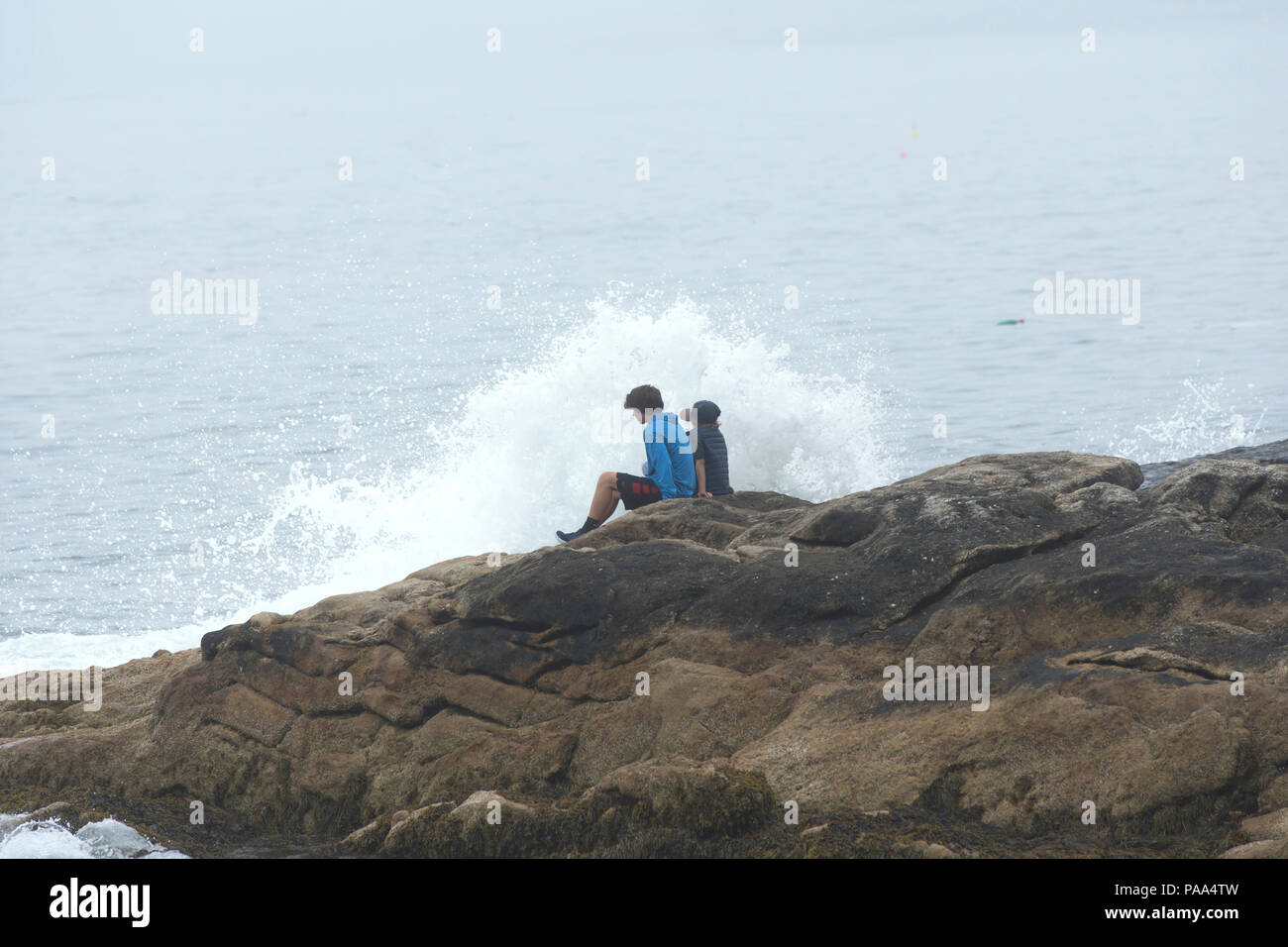 Due giovani ragazzi seduti sulle rocce vicino a rompere il surf nel punto dell'oceano, Boothbay, Maine, Stati Uniti d'America Foto Stock