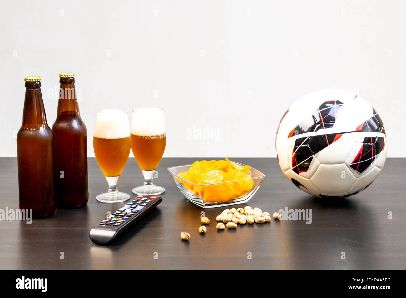 Persone preparate per guardare una partita di calcio in TV con la birra. Vi  è una birra sul tavolo, palla, il telecomando della TV, snack. La birra  artigianale. Sfondo chiaro Foto stock -