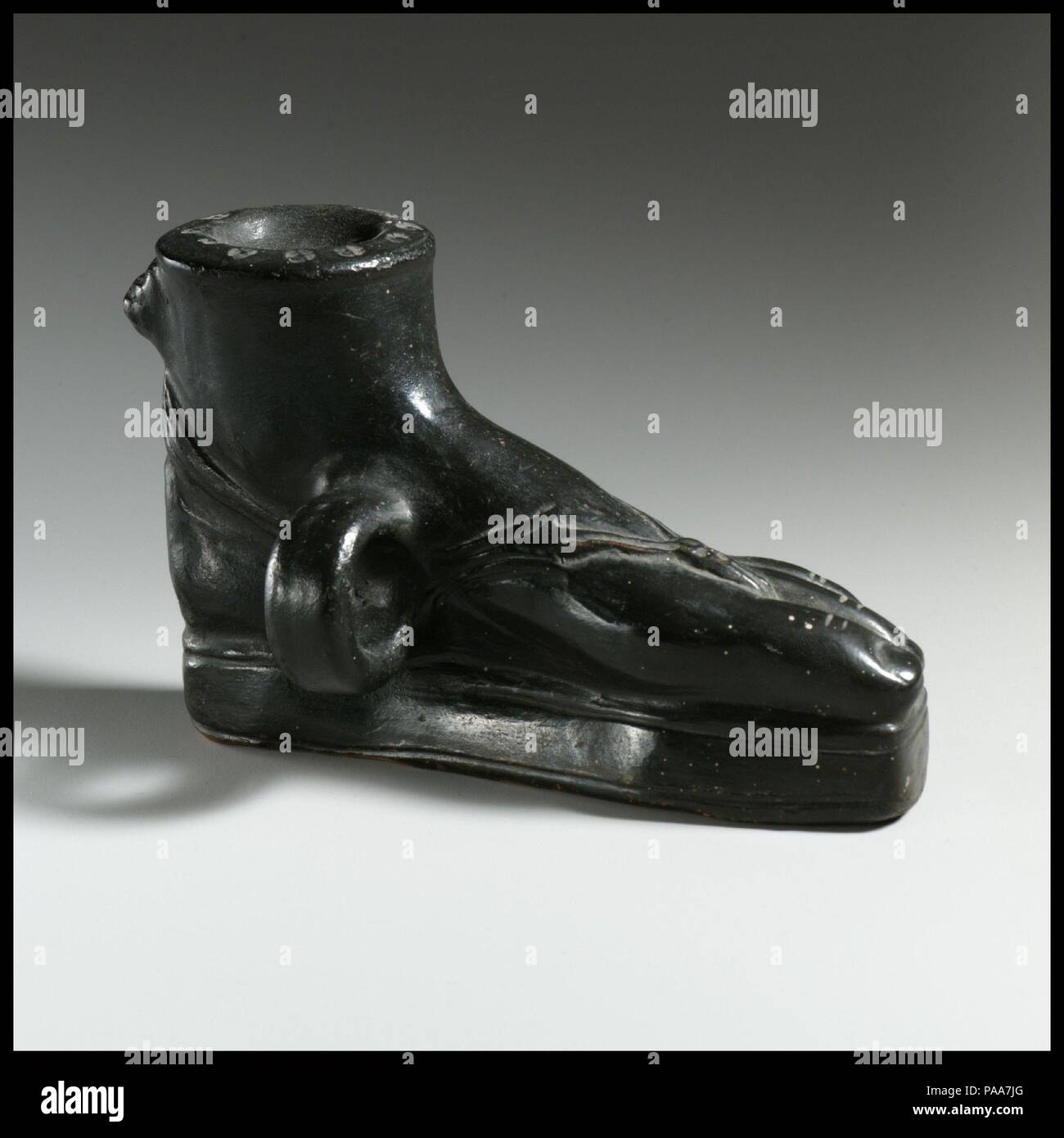 La terracotta guttus (pallone con manico e beccuccio). Cultura: greco, Sud italiano, quello campano. Dimensioni: H. 3 1/2 in. (8,9 cm) di lunghezza 5 1/8 in. (13 cm). Data: Del IV secolo A.C. Il piede sinistro indossa un sandalo con una spessa suola - forse quella di un attore? Le caratteristiche funzionali dell'oggetto includono la succhieruola nella parte superiore, un piccolo tubo in forma di una testa di leone, e l'anello verticale maniglia. Vasi in forma di piedi sandaled si verificano in arte greca in tutte le epoche e in tutti i settori. Museo: Metropolitan Museum of Art di New York, Stati Uniti d'America. Foto Stock