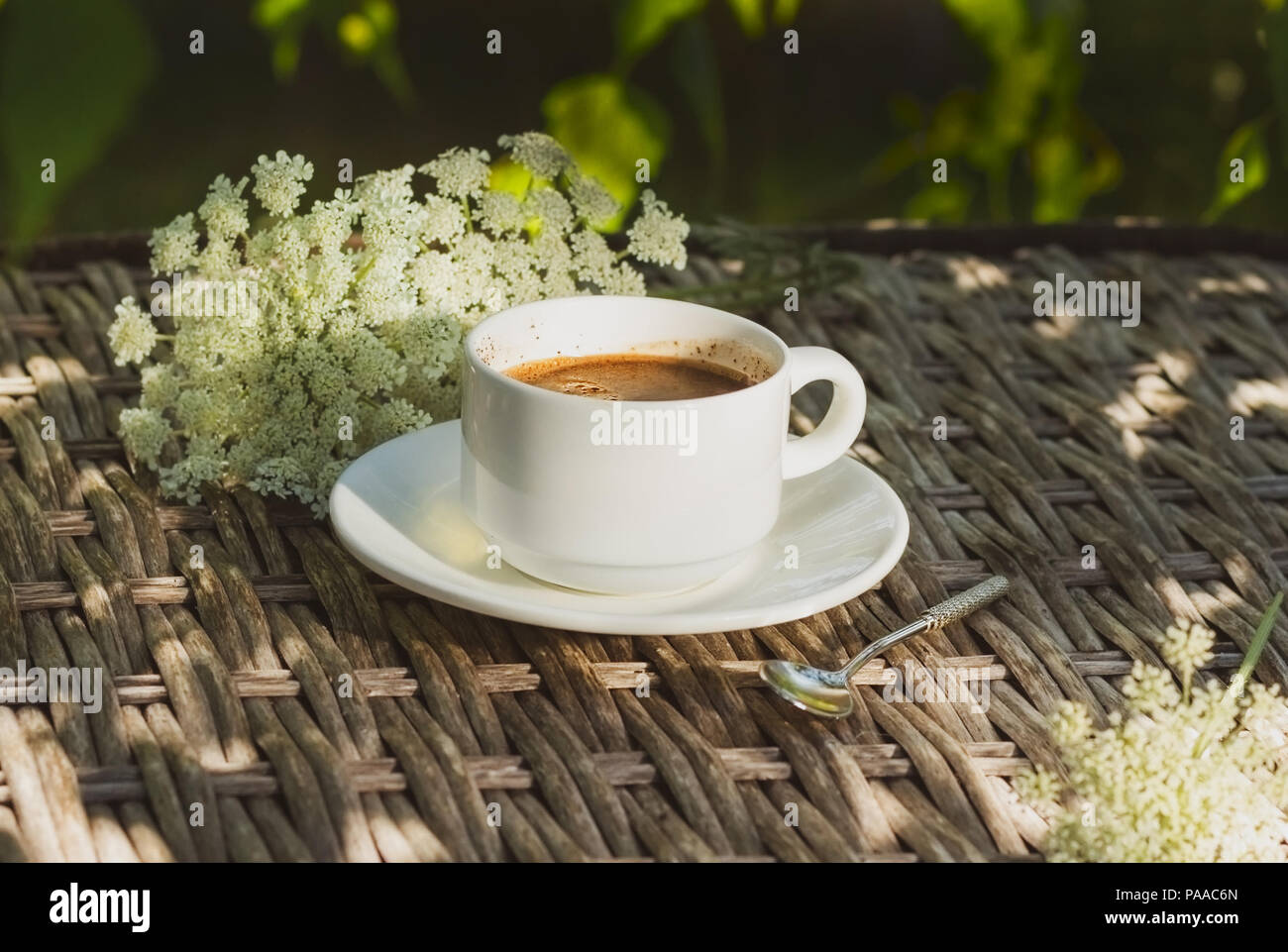 Una tazza di caffè su una tabella di vimini su uno sfondo di fiori Foto Stock