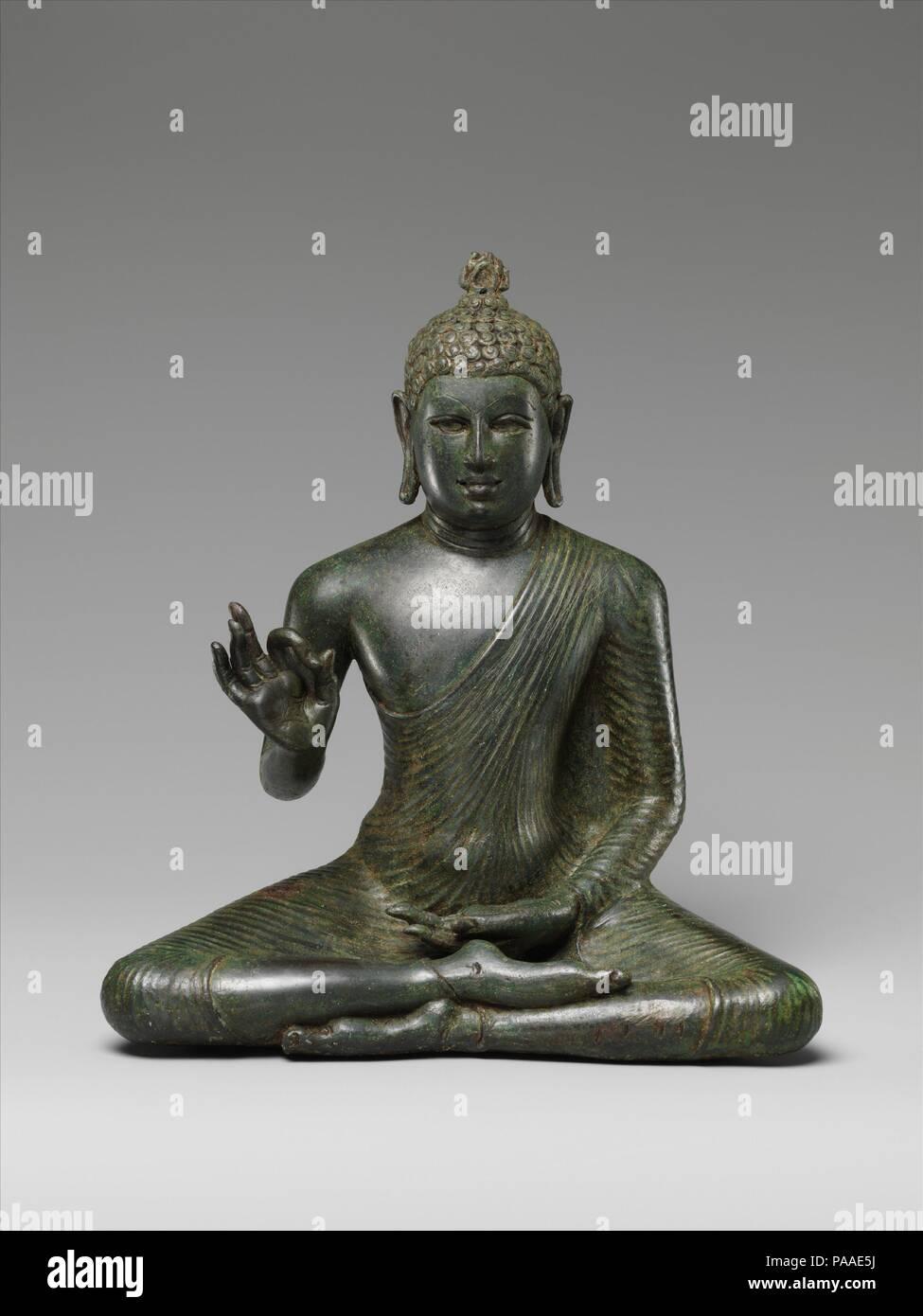Il Buddha enunciare il Dharma. Cultura: Sri Lanka (Anuradhapura). Dimensioni: H. 10 1/2 in. (26,7 cm); W. 11 a. (7,9 cm); D. 4 1/2 in. (11,4 cm). Data: fine VIII secolo. La quintessenza dell'icona di inizio dei buddisti dello Sri Lanka è il Buddha gesticolando vitarka-mudra, impartendo il suo dharma a tutti. Seduti in meditazione yogic postura, indossa il monaco's uttarasanga, un untailored lunghezza del panno tautly disegnata attorno al corpo con la sua spalla destra esposta in modo meridionale del buddismo. Il suo pelo è espresso in breve, riccioli di evocare la sua rinuncia del mondo materiale, quando ha tagliato h Foto Stock