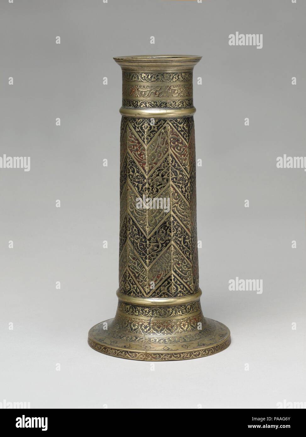 Lampada inciso Stand con Chevron Pattern. Dimensioni: H. 13 1/4 in. (33,7 cm) Diam. (Base) 6 5/8 in. (16,8 cm). Data: datato A.H. 986/ A.D. 1578-79. La poesia inscritta intorno a questa lampada stand esprime mistica sufi sentimenti. Lirica versi dal Bustan (frutteto) dei Sa'di sono collocati in tre a forma di zig-zag registri che copre l'albero: Mi ricordo di una notte come i miei occhi non dormire ho sentito una falena che parla con una candela. [Detta la falena:] "Perché io sono un amante è [solo] diritto che mi dovrebbe bruciare. [Ma] perché dovreste piangere e masterizzazione di te?". Museo: Metropolitan Museum of Art Foto Stock