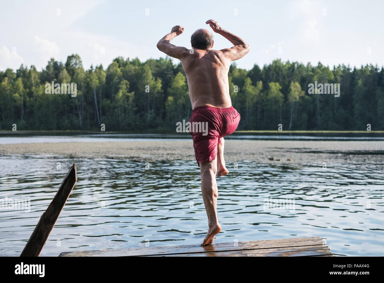 Uomo maturo in rosso il costume saltando nel lago. avente un buon riposo outdoor in vullage Foto Stock