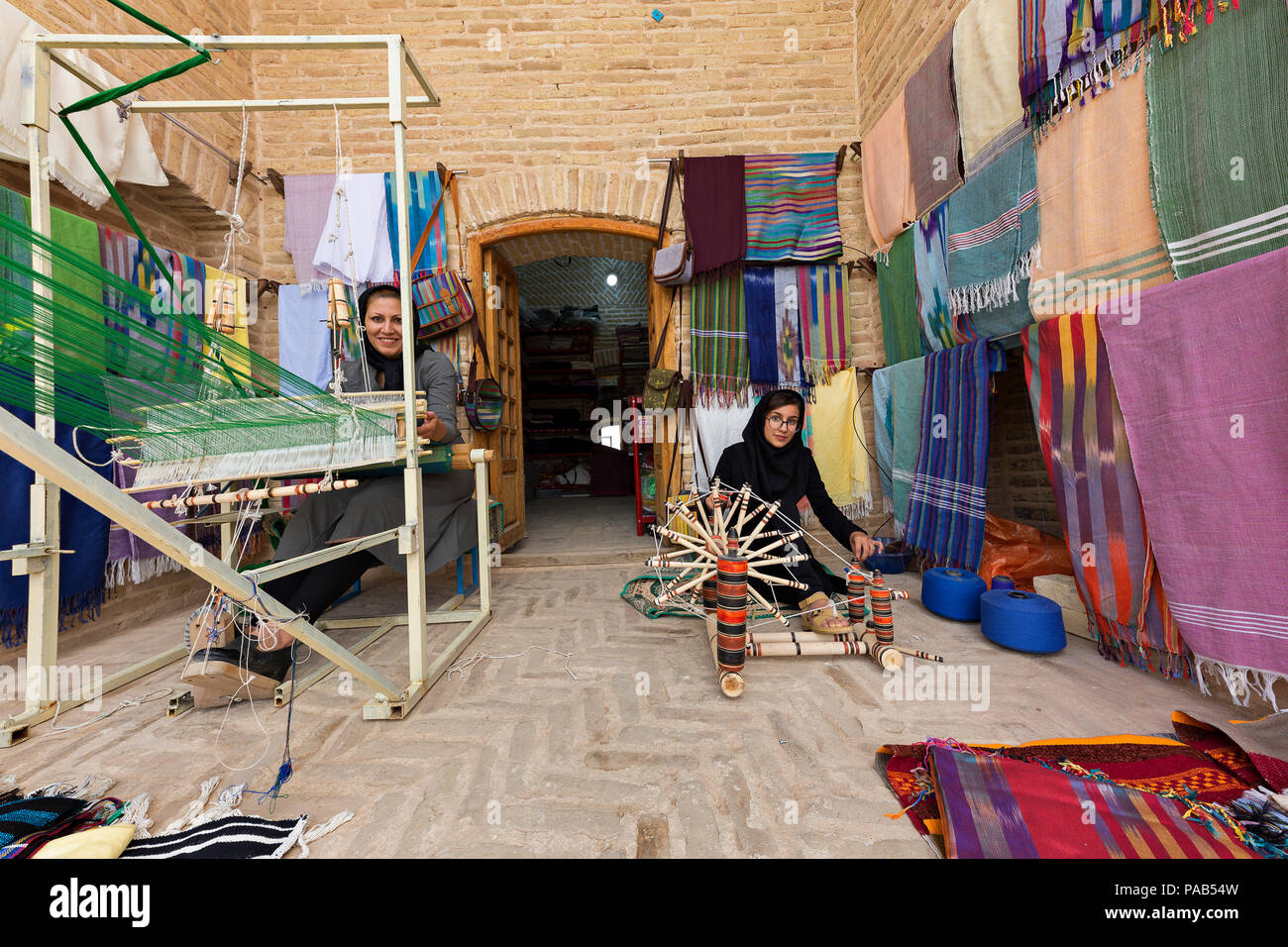 La donna si intreccia con il tessuto in modo tradizionale e un'altra donna gira la lana, in Meybod, Iran. Foto Stock