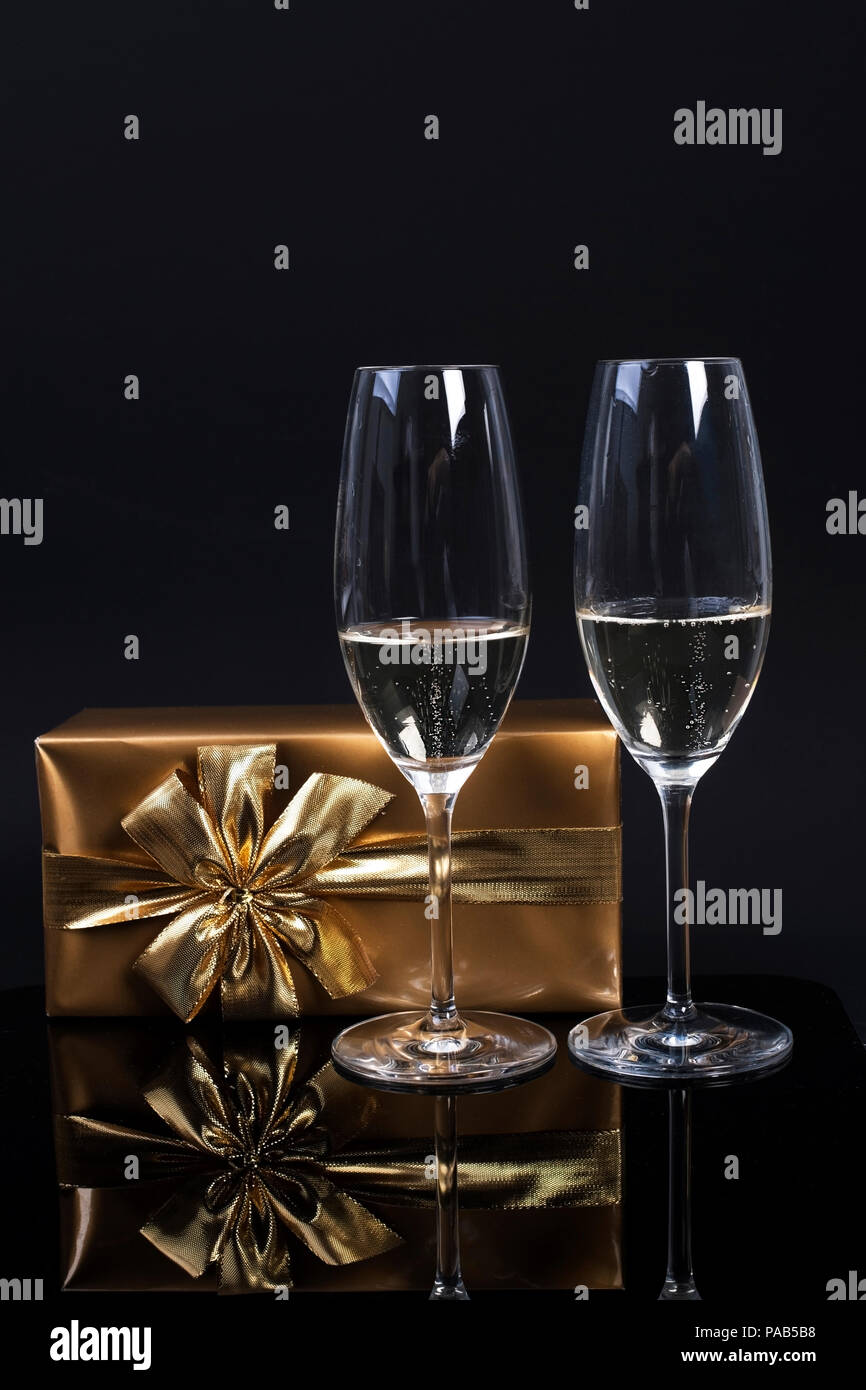 Due bicchieri di champagne, un regalo in carta oro con un arco e una  maschera di Carnevale su sfondo nero Foto stock - Alamy