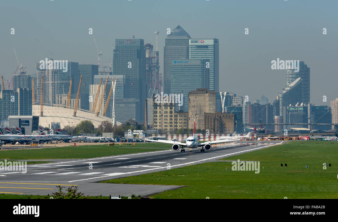 Airbus A220-100 l'atterraggio all'Aeroporto di London City con le torri di Canary Wharf e l'O2 in background Foto Stock