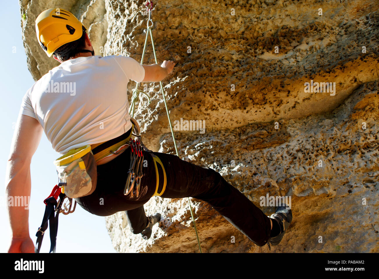 Foto dal retro del turista uomo nel casco e T-shirt bianco a salire in montagna a top Foto Stock