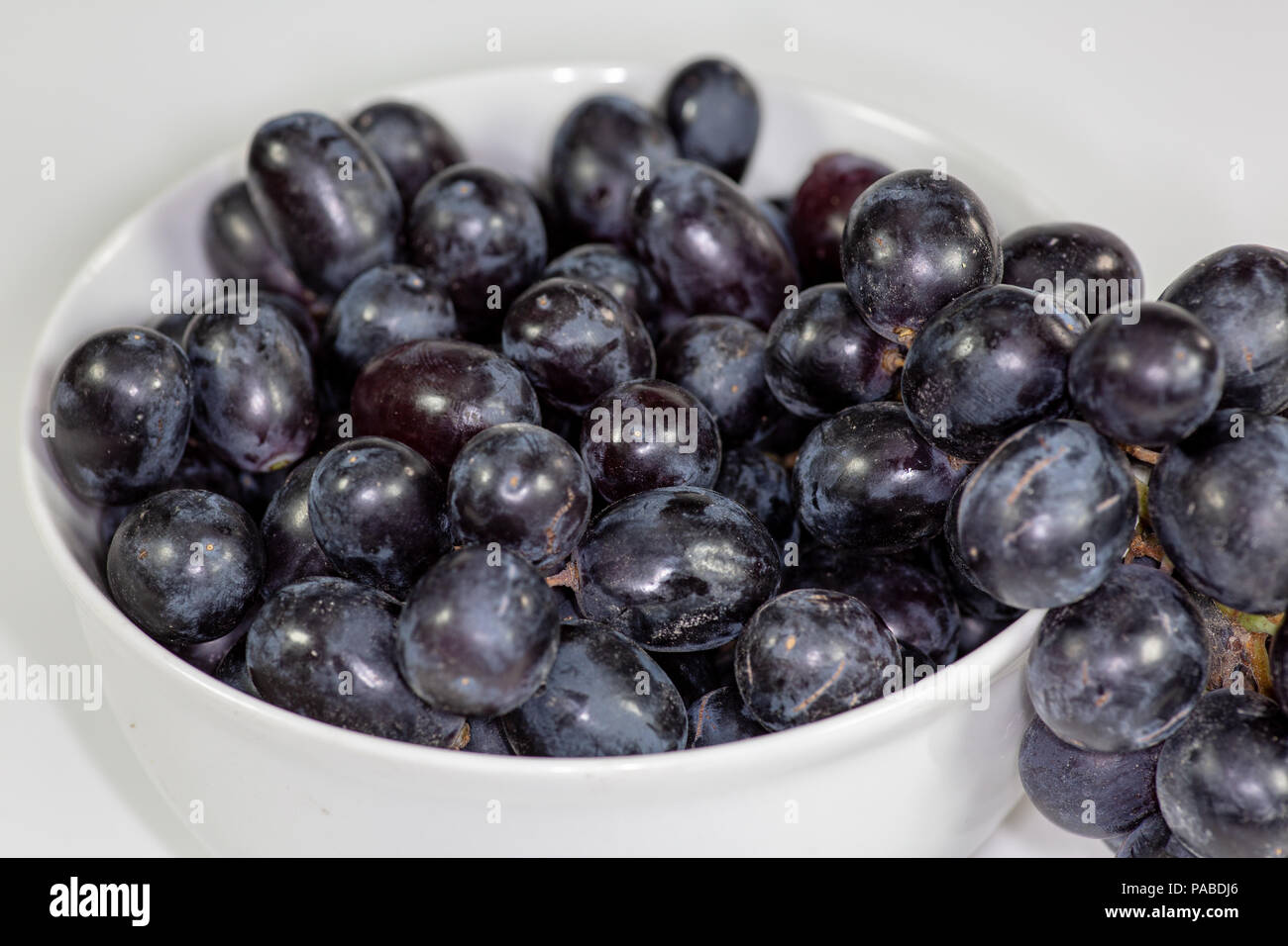 Uva nera in una profonda coppa bianco su un racconto bianco in attesa di essere consumati Foto Stock