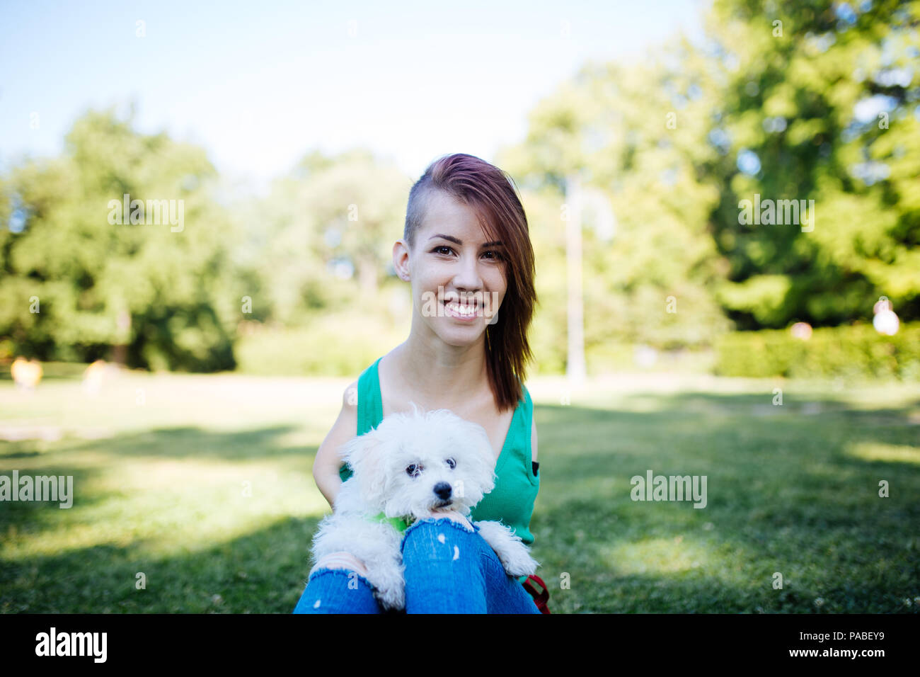 Ritratto di bella non valido sorridente ragazza nata senza arti superiori godendo con il suo piccolo cucciolo bianco nel parco. Foto Stock