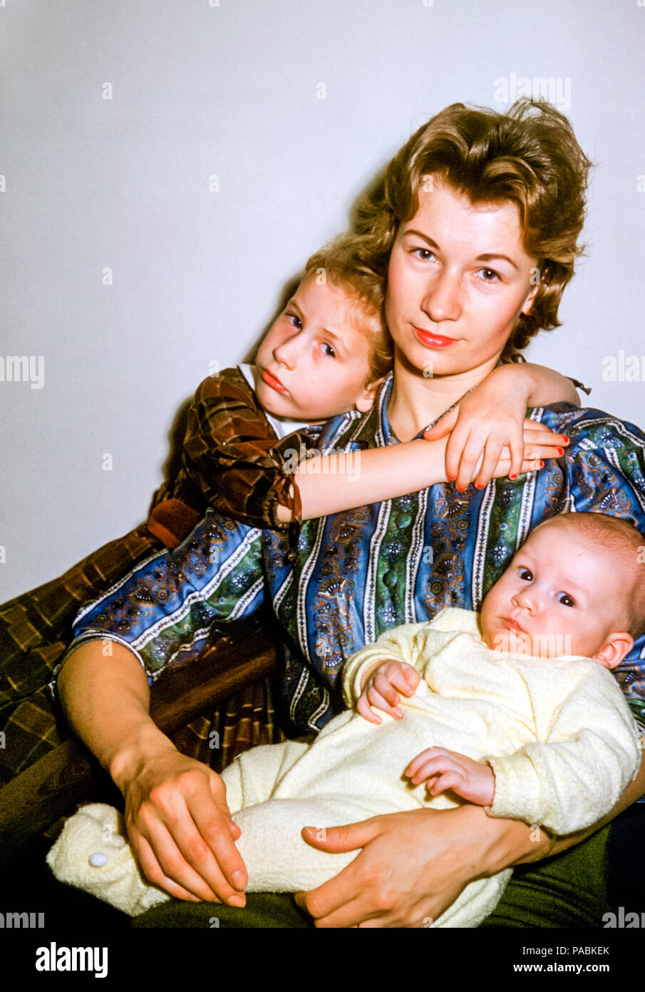 Ritratto di famiglia di madre e due figli negli Stati Uniti negli anni '60.  La giovane donna ha capelli biondi e indossa rossetto rosso. La bambina  bionda di 4 anni abbraccia la