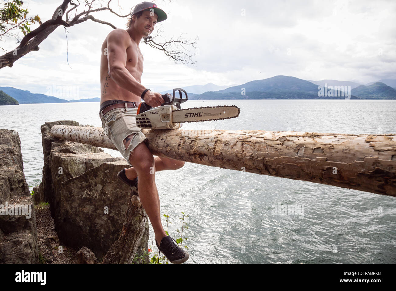 I Lions Bay, British Columbia, Canada - Luglio 1, 2018: l'uomo con un chainsaw è il taglio di un pezzo di legno per costruire un cliff jumping piattaforma. Foto Stock