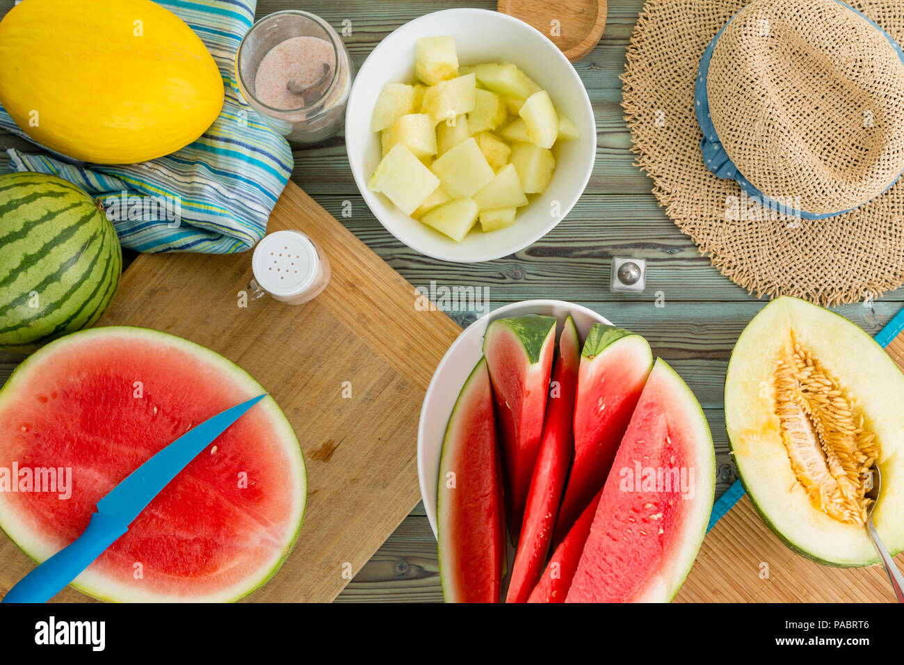 Estate ancora la vita di un tavolo da picnic con fresco affettato luminoso giallo canarino melone e fette di cocomero, intero e dimezzato la frutta e un rustico di paglia s Foto Stock