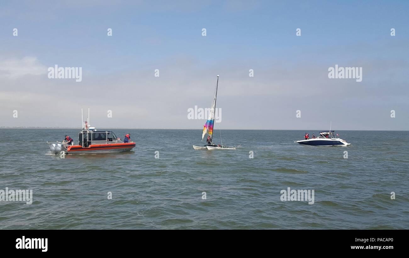 La guardia costiera gli equipaggi in barca lungo con un Coast Guard barca ausiliaria equipaggio aiutare un diportista più dopo il suo 15-piede catamarano capovolto in Bolivar spiaggia piccola barca tagliare, 13 marzo 2016. (U.S. Coast Guard foto di Sottufficiali di terza classe Brandon Gonzalez) Foto Stock