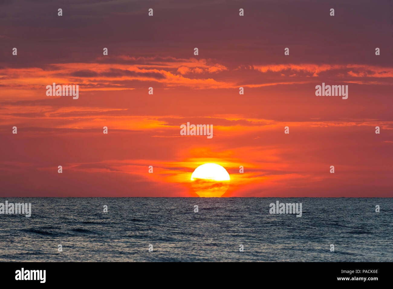 Sun andando giù parially dietro le nuvole in cielo arancione sull'acqua nel Golfo del Messico Foto Stock
