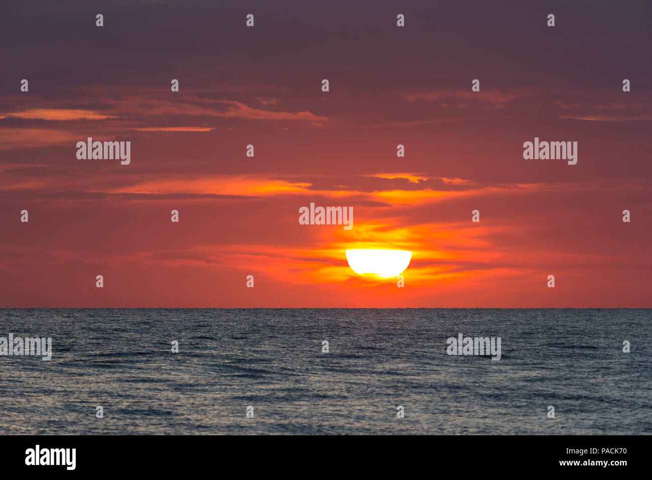 Sun andando giù parially dietro le nuvole in cielo arancione sull'acqua nel Golfo del Messico Foto Stock