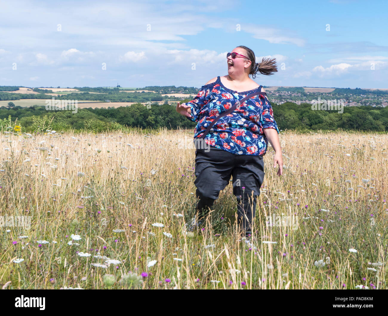 Giovane donna salta e gira intorno ad un prato in campagna britannica in un giorno caldo nel luglio 2018 ondata di caldo a Highdown Hill, West Sussex, in Inghilterra, Regno Unito. Concetto di felicità. Essere felice concetto. Jumping con gioia il concetto. Foto Stock