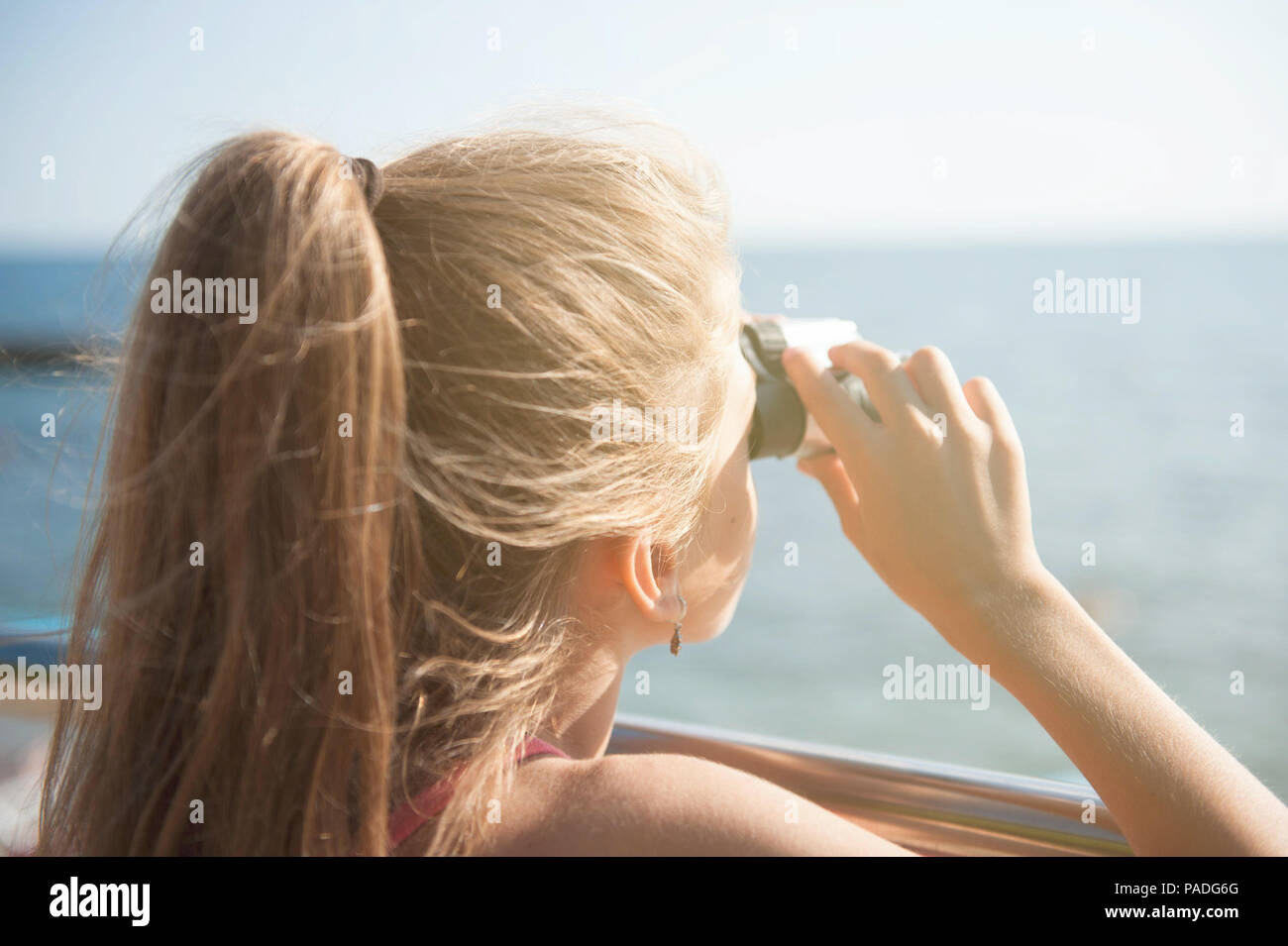 Sognando piccola ragazza con i capelli lunghi tenendo il binocolo cercando sul mare orizzonte Foto Stock