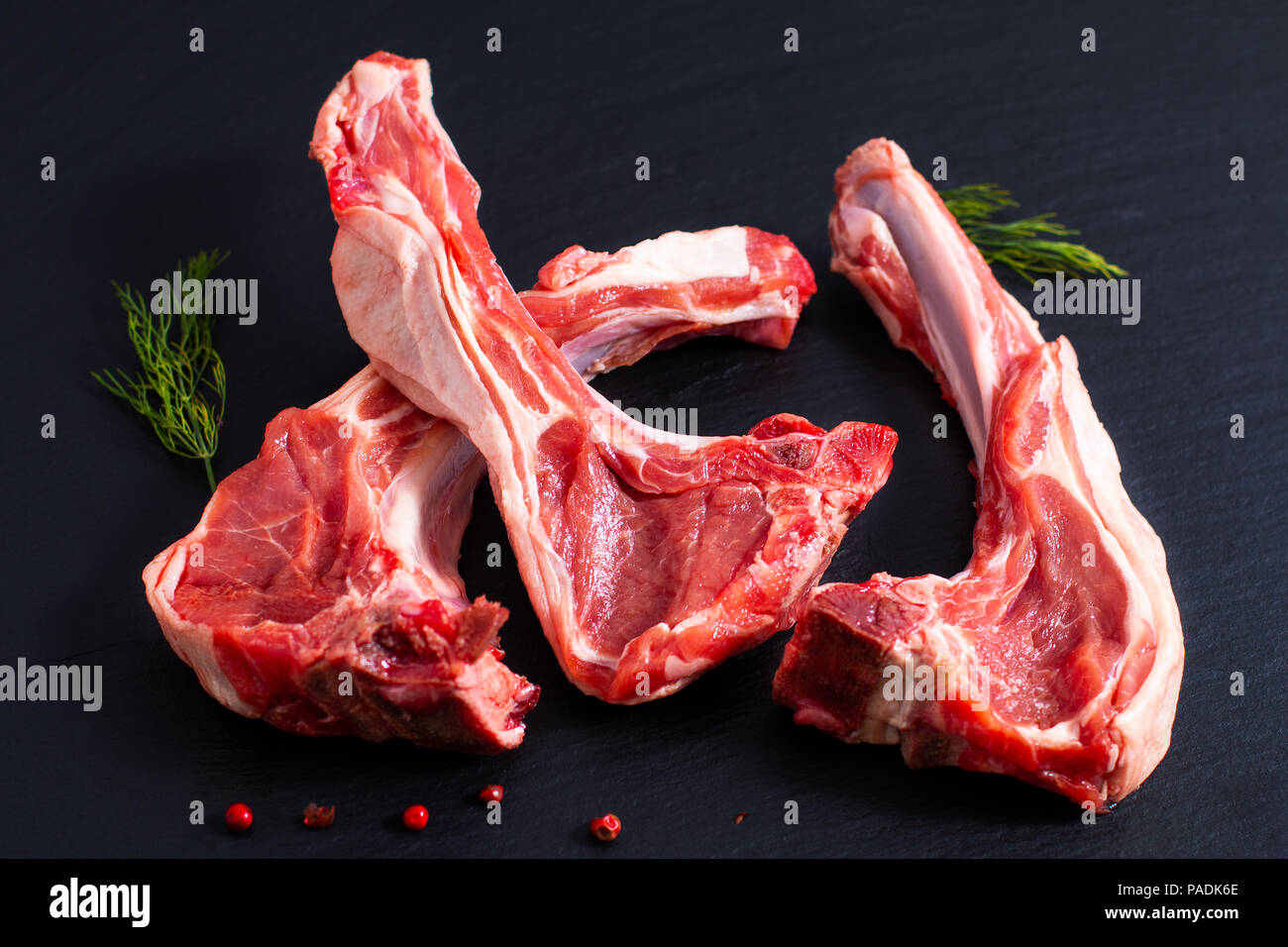 Concetto di cibo organico costolette di agnello su ardesia nera pietra con erbe Foto Stock