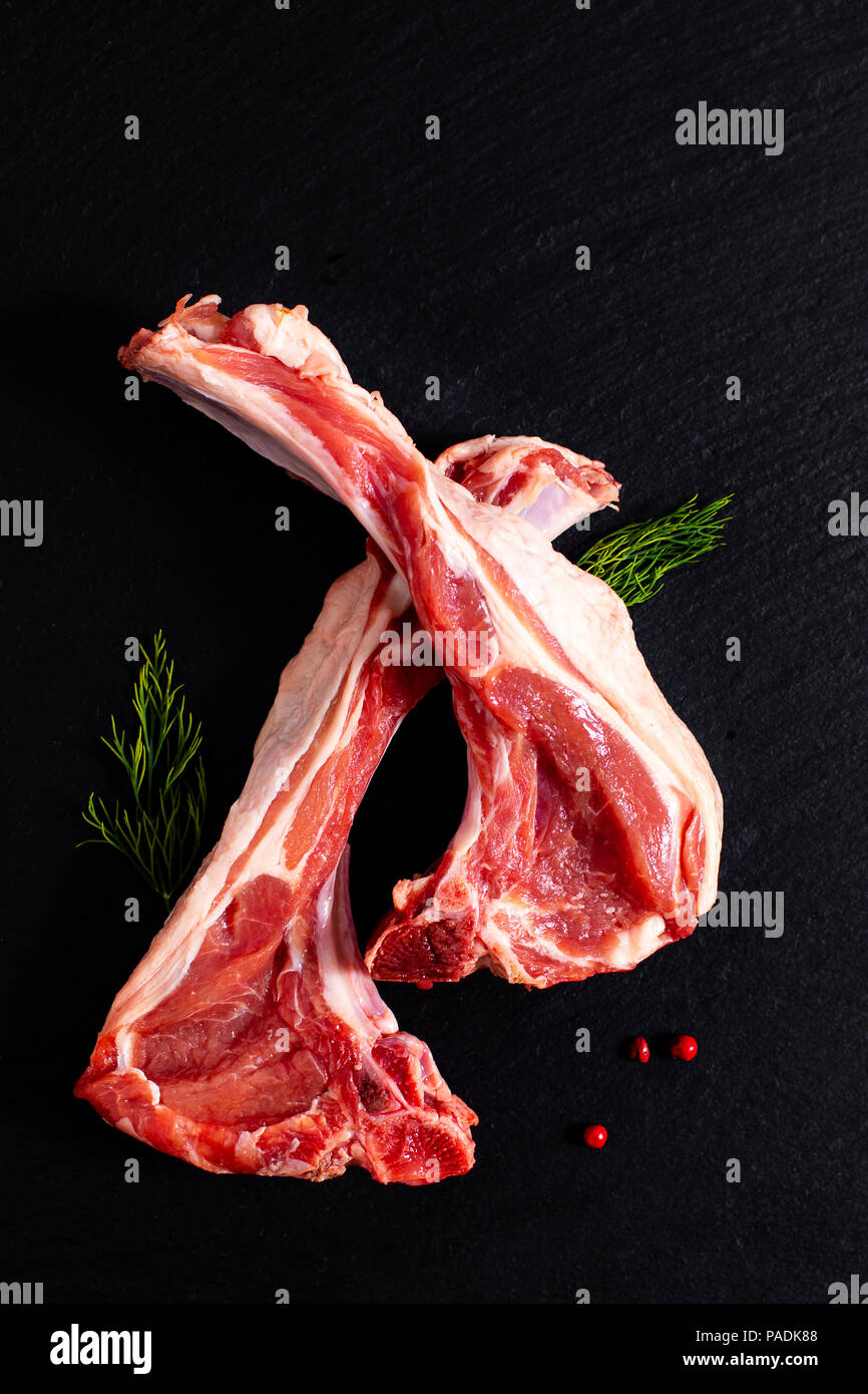 Concetto di cibo organico costolette di agnello su ardesia nera pietra con erbe Foto Stock