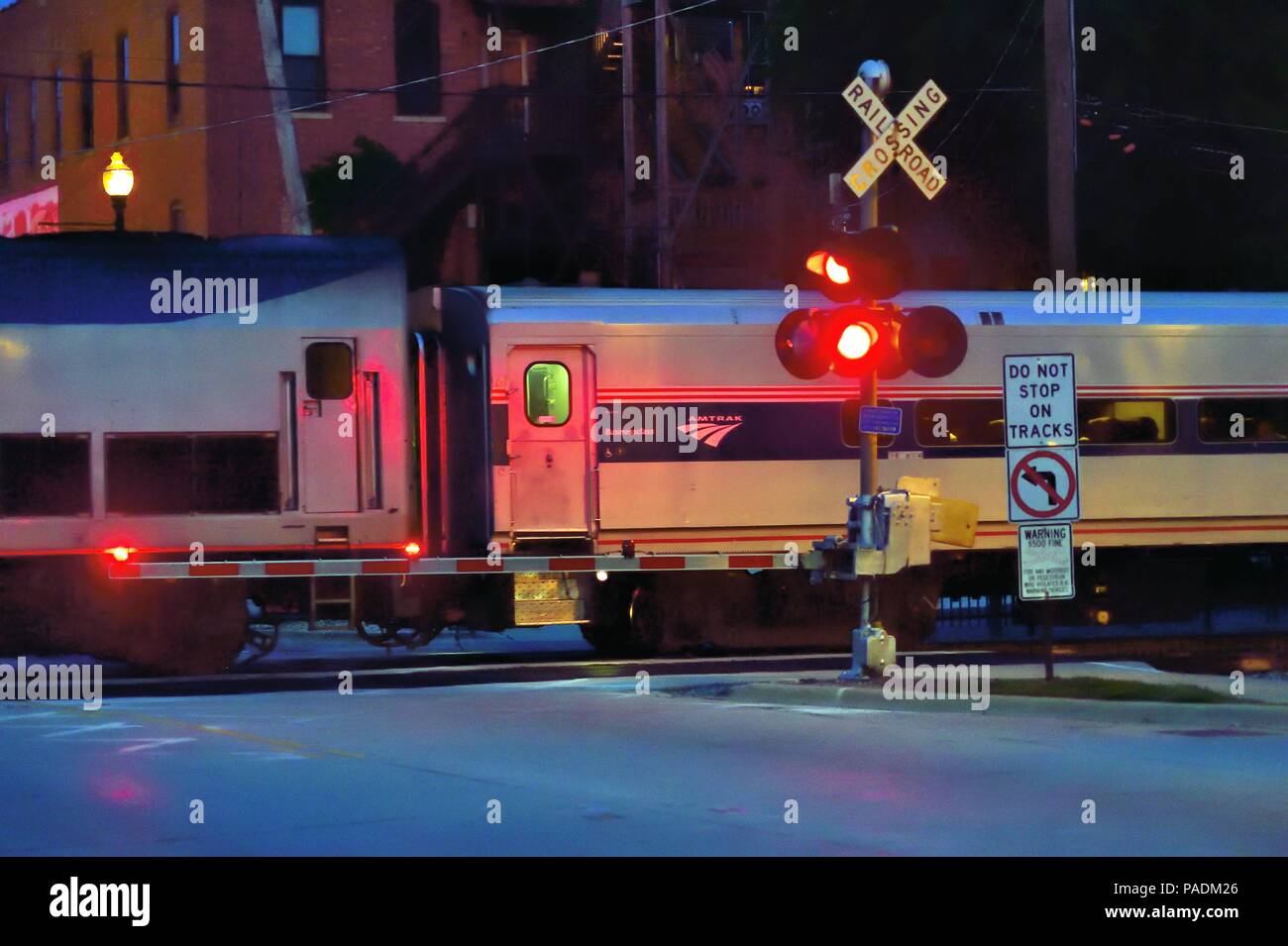 Lockport, Illinois, Stati Uniti d'America. Un Amtrak treni passeggeri destinati a Chicago passando attraverso un grado incrocio dopo scuro su una notte d'estate. Foto Stock