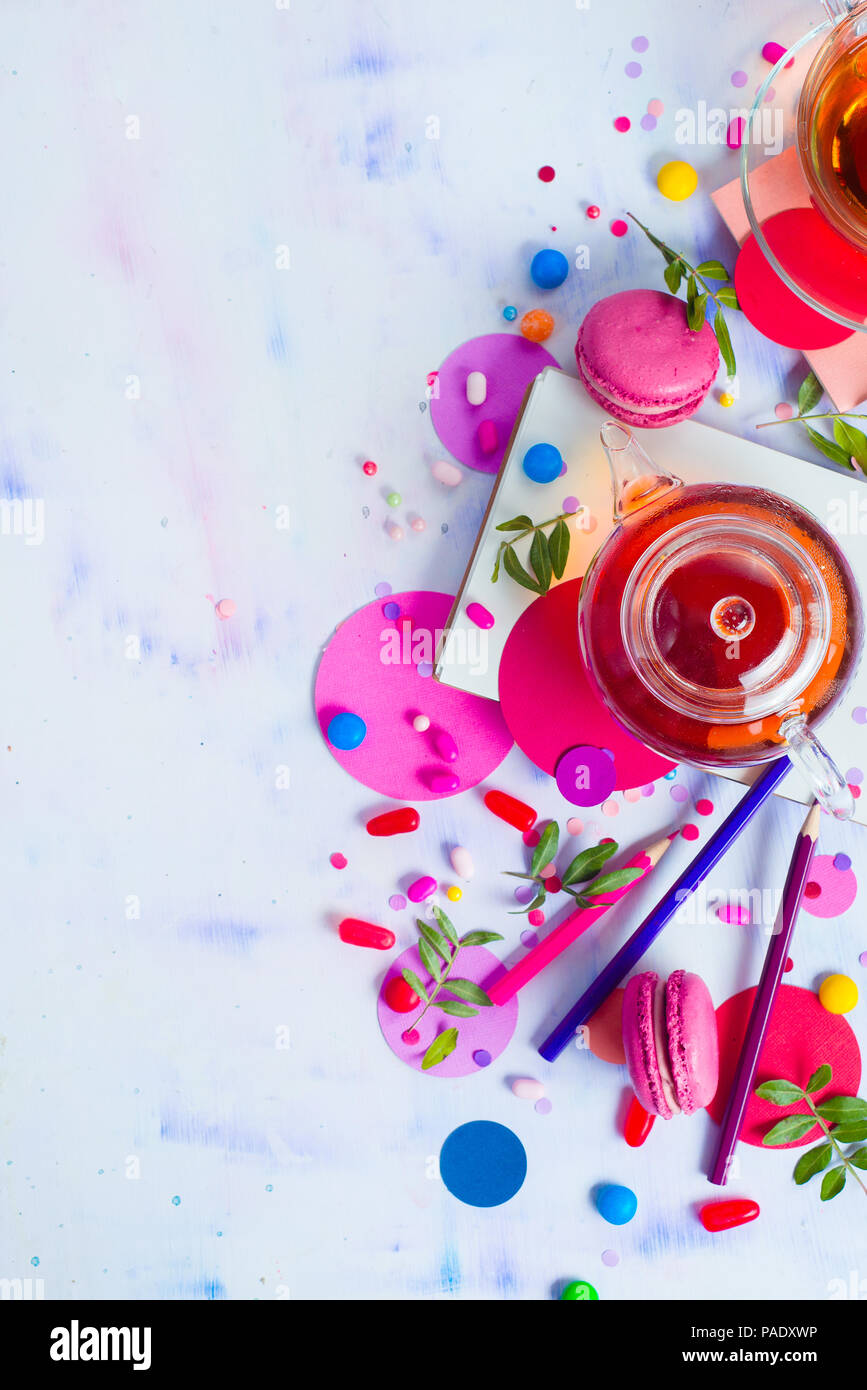 Teiera in vetro con caramelle e coriandoli su uno sfondo luminoso con copia spazio. Rosa e viola tavolozza ancora in vita. La vibrante tea party drink laici piana. Foto Stock