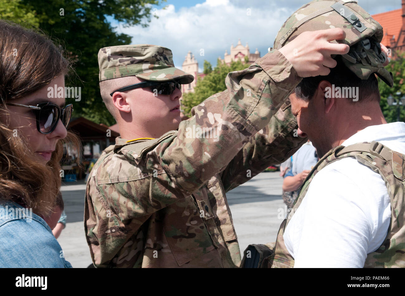 Spc. Patrick Dawson, da Peoria, Illinois, con la XVIII Polizia Militare Brigata aiuta un cittadino polacco don l'esterno migliorato gilet tattico e Army combat casco durante la visualizzazione statica a una giornata multiculturale evento nella piazza della città di Chelmno, Polonia, come una parte di esercizio Anakonda 2016. Esercizio Anakonda 2016 è il principale evento di formazione per gli Stati Uniti Esercito e l'Europa delle nazioni partecipanti e dimostra come gli Stati Uniti e i paesi partner possono efficacemente unità insieme sotto un comando unificato mentre la formazione su un scenario contemporaneo. Foto Stock