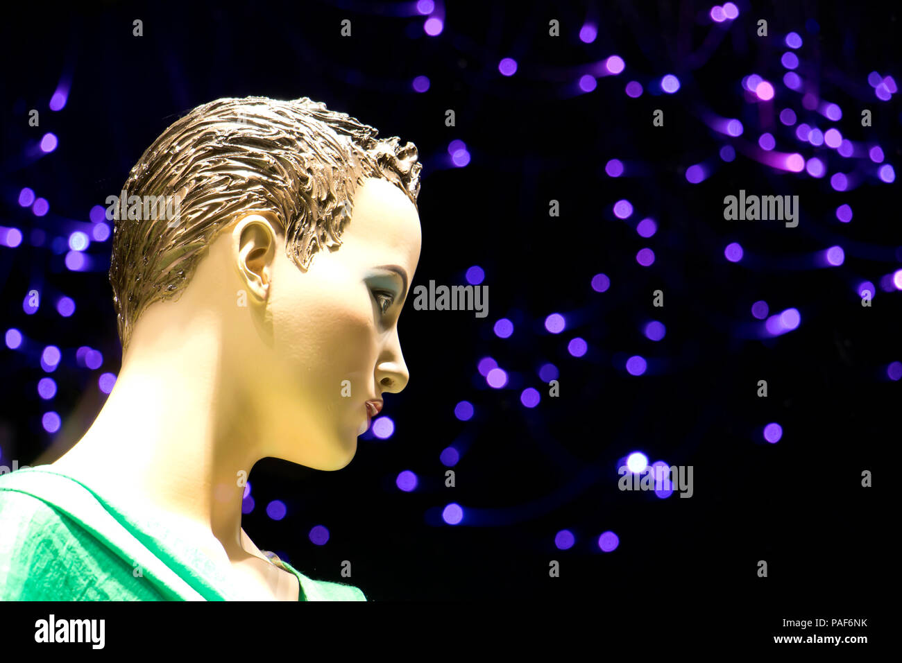 In prossimità di una femmina mannequin doll visualizzato n la vetrina del negozio con sfocate luci viola in background , vista di profilo Foto Stock