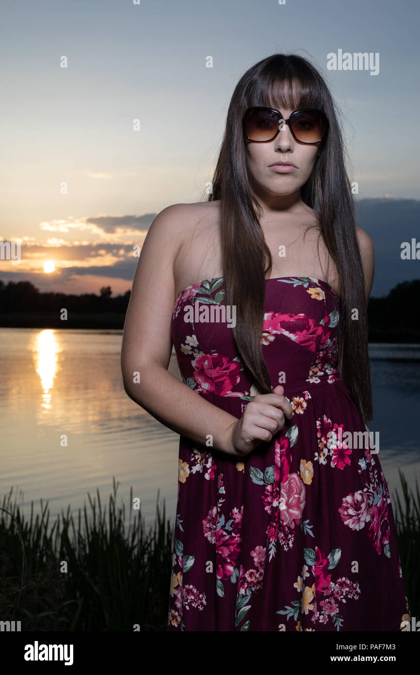 Lo spagnolo donna americana in piedi sul bordo di un lago in  Cambridgeshire. Indossando una susina colorati abiti floreali e occhiali da  sole durante un tramonto d'estate Foto stock - Alamy