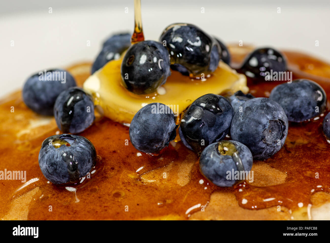 Sciroppo di versamento al di sopra del burro sul mirtillo pila di frittelle sul tavolo della cucina in attesa di essere consumati Foto Stock