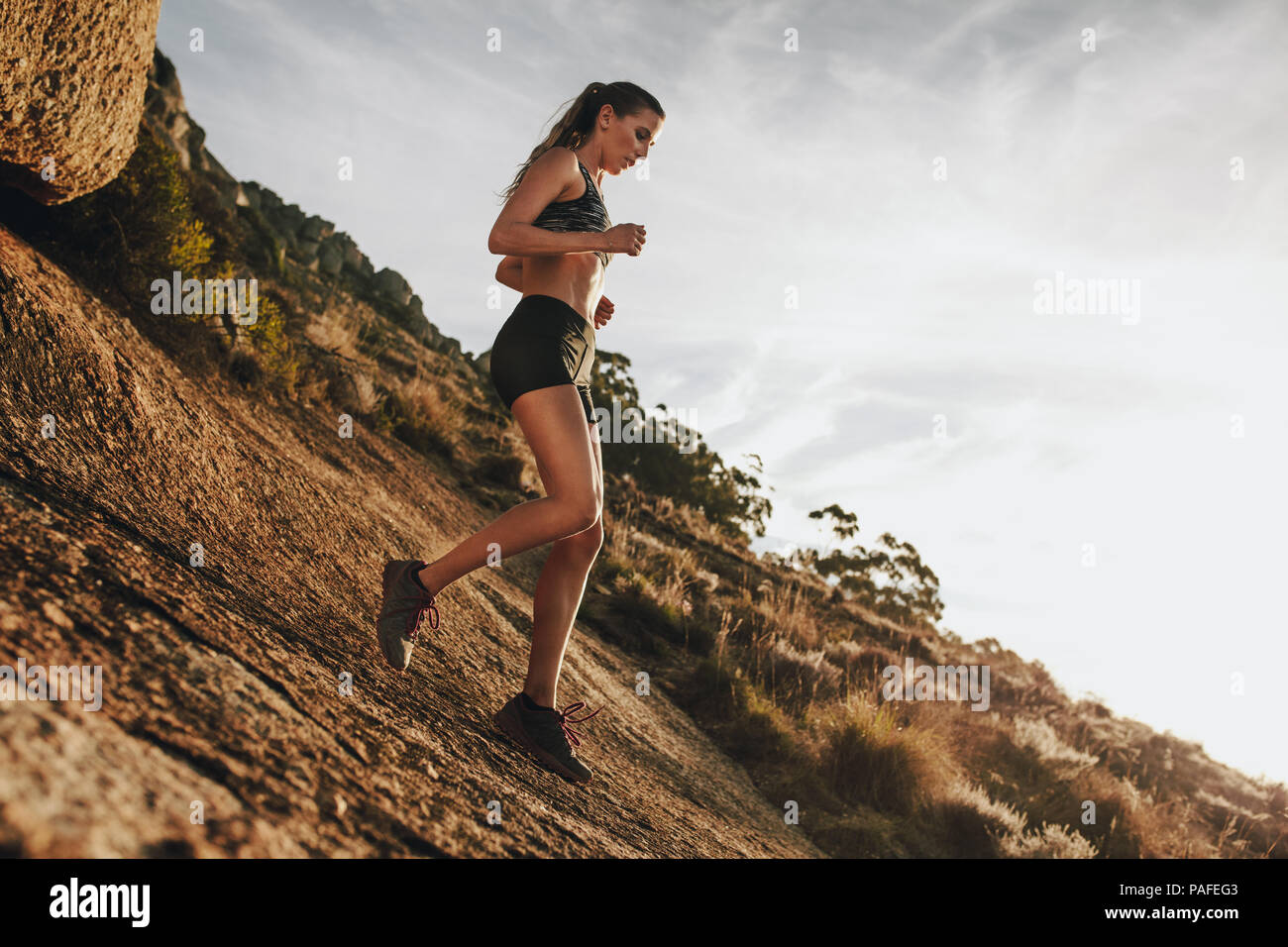 donna sportiva che corre in discesa su un sentiero roccioso di montagna. Atleta di trail runner che si allena per una corsa in discesa. Foto Stock