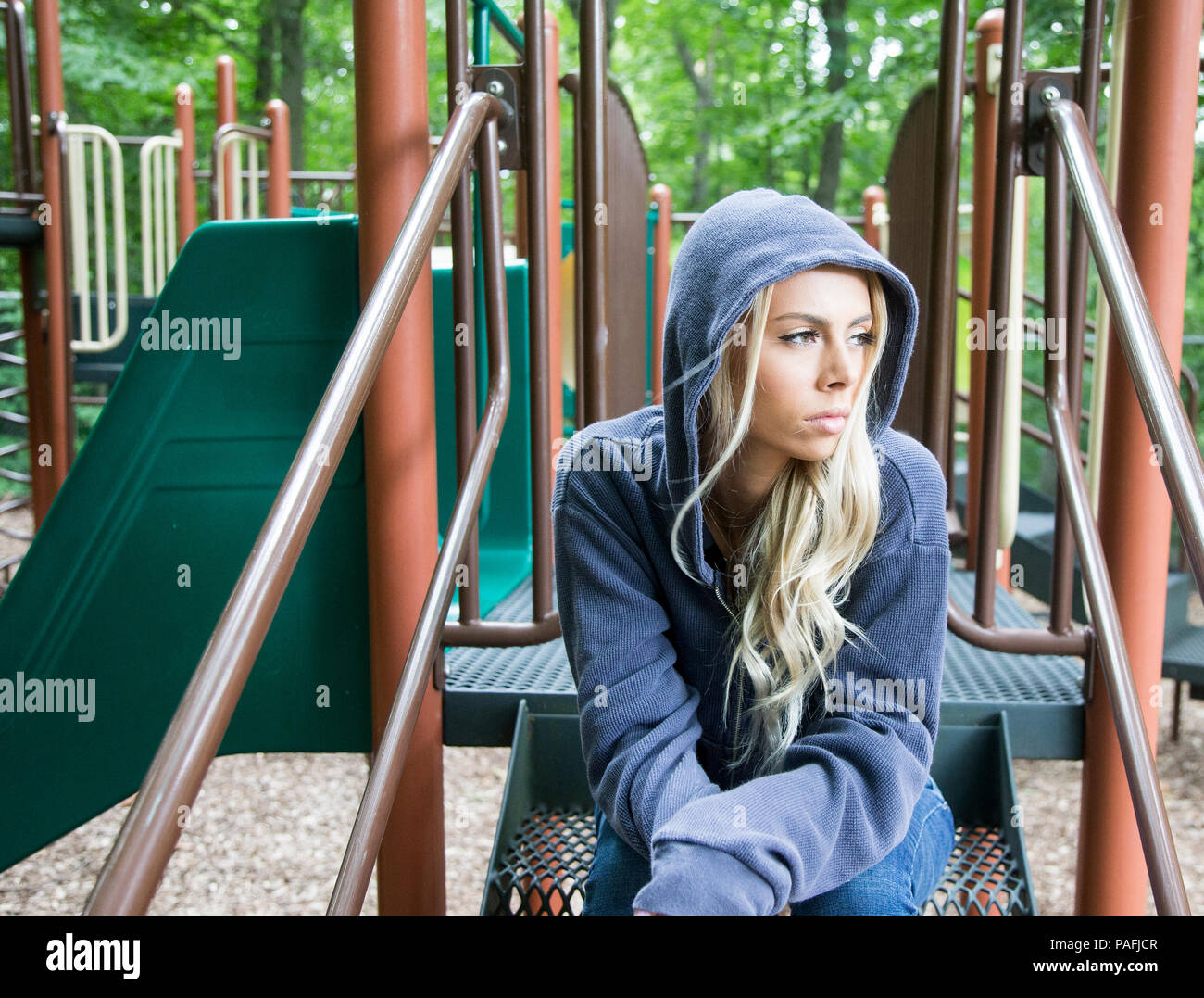 Ragazza seduta a un parco giochi in un cupo umore Foto Stock