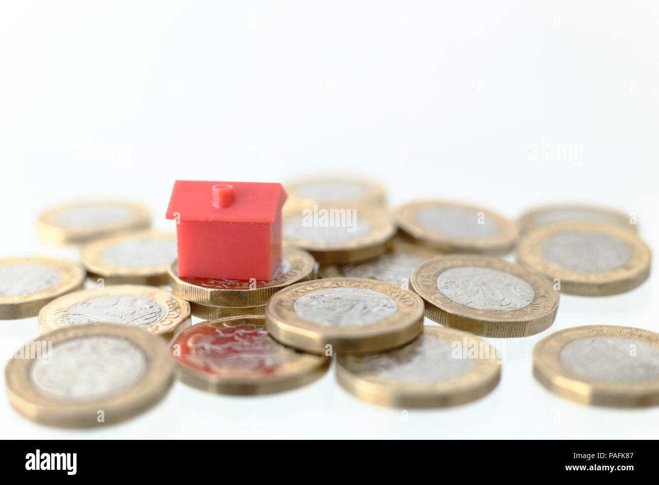 Rosso casa di plastica su un mucchio di nuove Uk Pound monete. Foto Stock