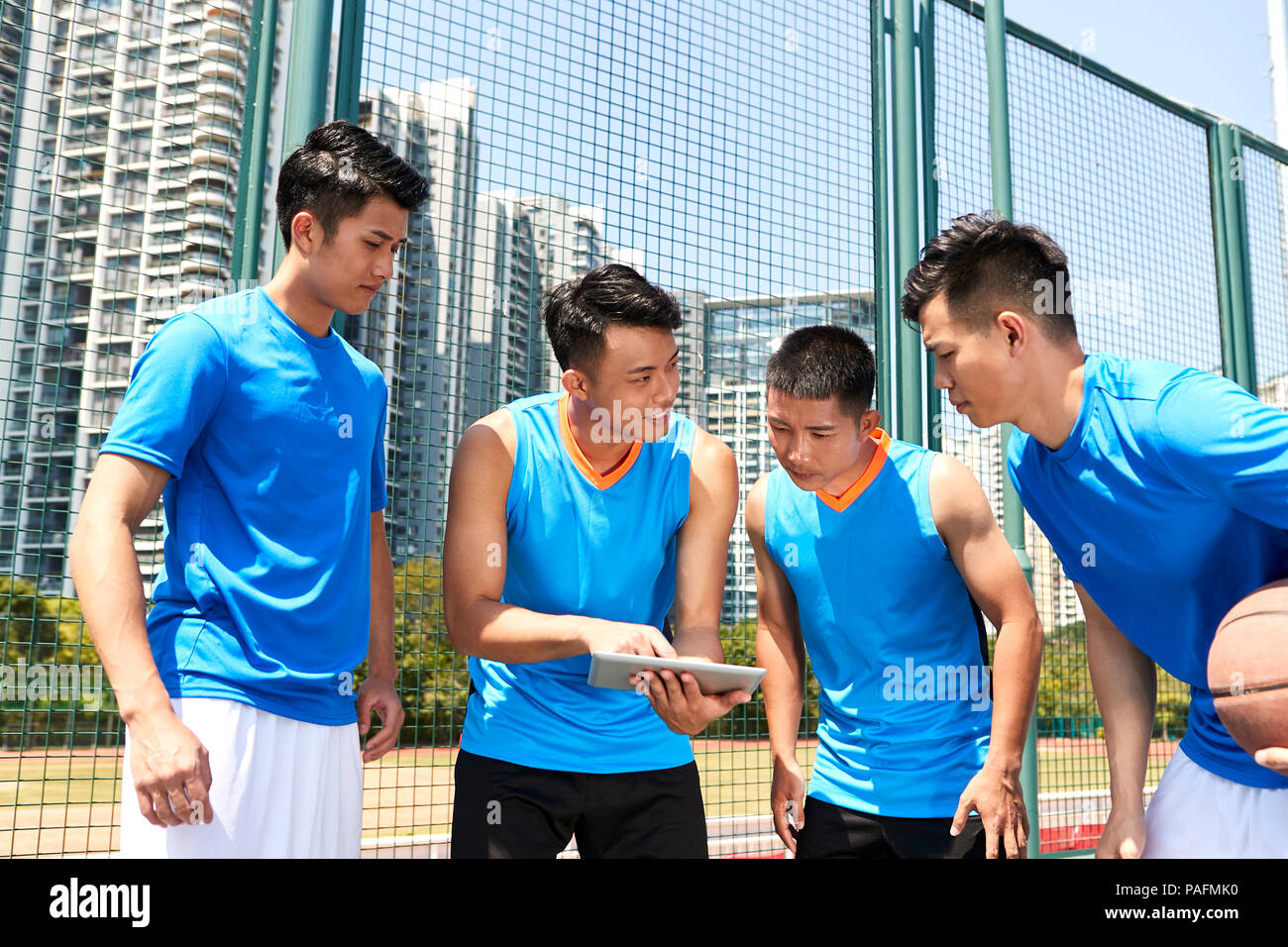 Giovani asiatici giocatori di basket a discutere di tattiche utilizzando tavoletta digitale a corte lato. Foto Stock