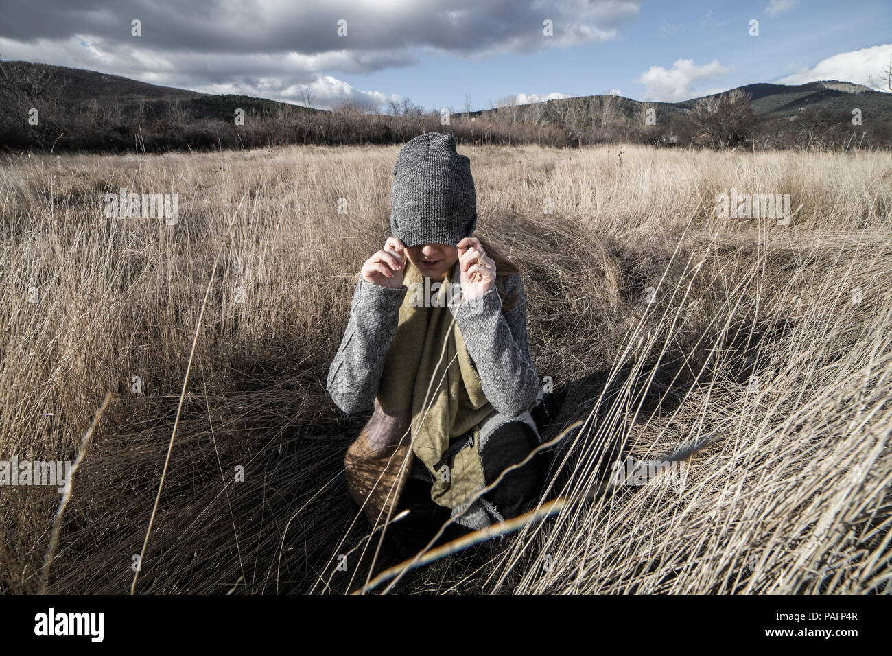 La donna in un secco campo di grano con gli occhi coperti con un tappo grigio Foto Stock